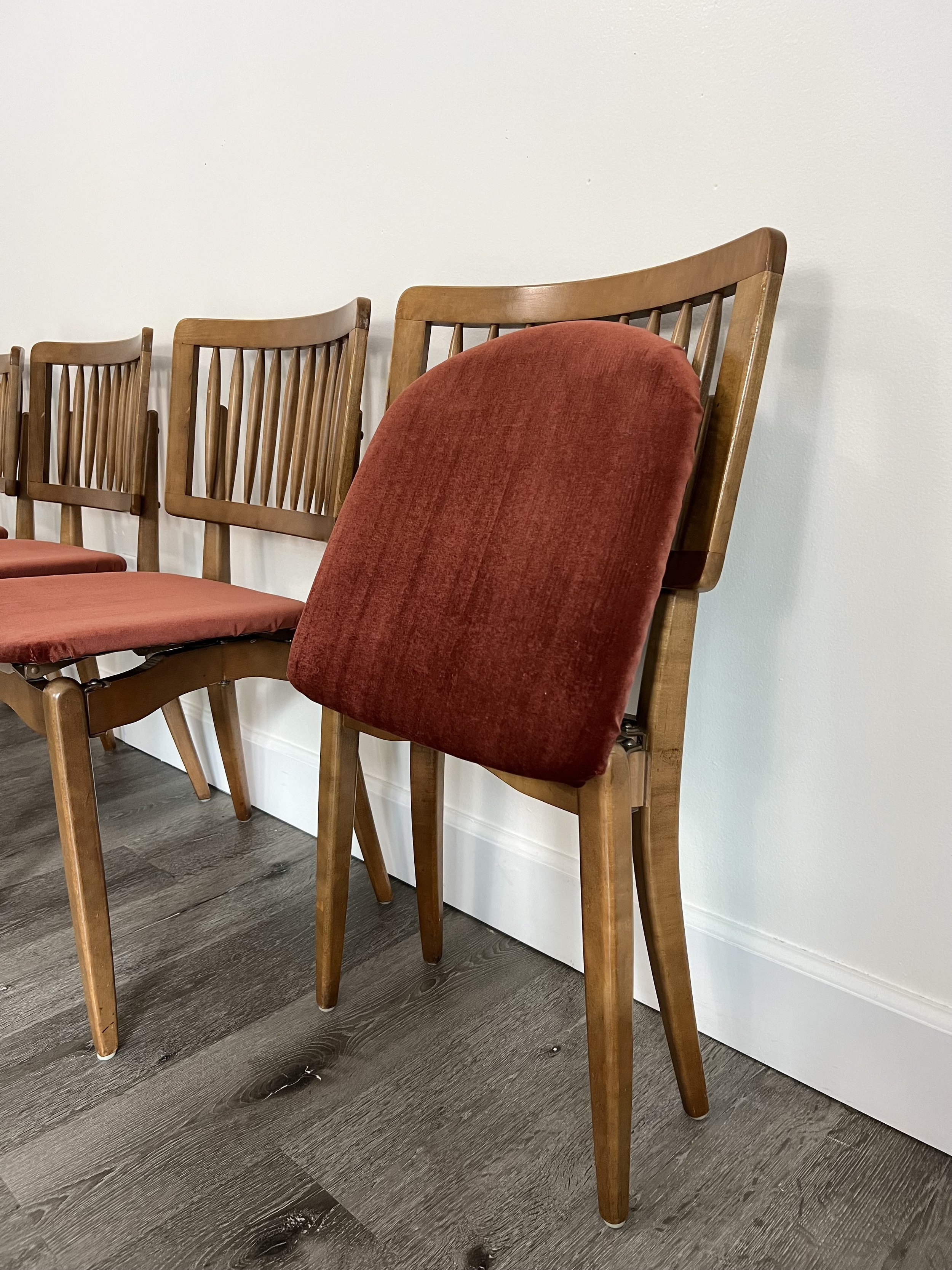 A row of wooden chairs with red upholstered seats and backrests, set against a white wall.
