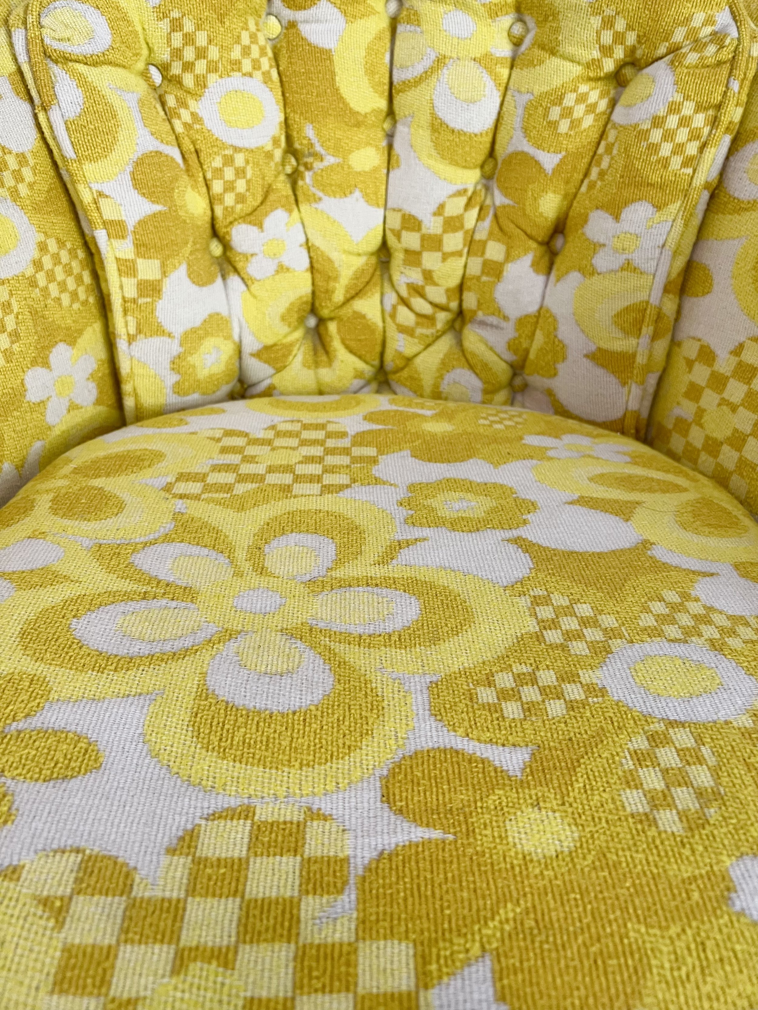 Close-up view of a vintage yellow and white floral patterned upholstered chair or armchair with tufted backrest and decorative buttons.