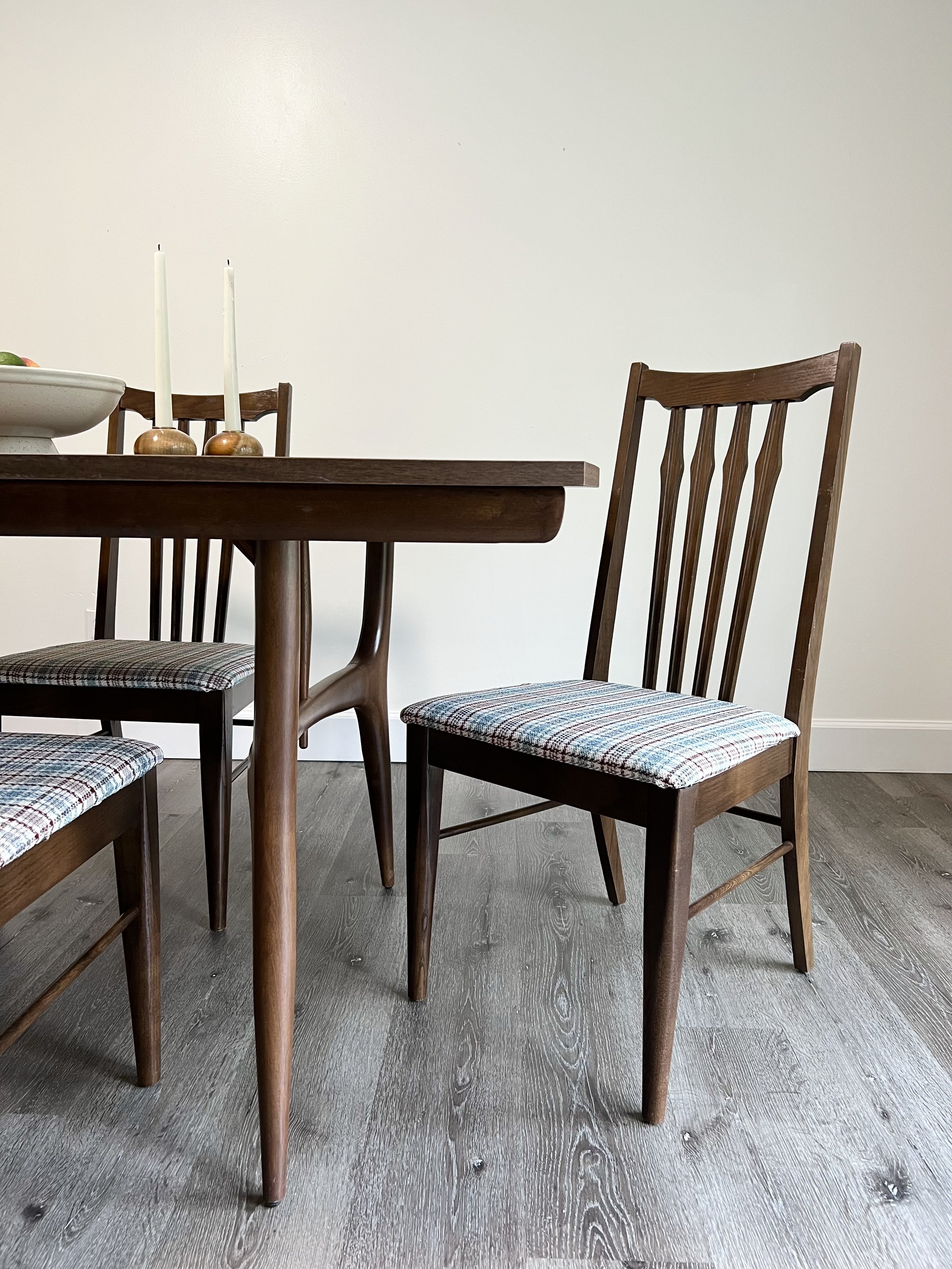 A dining room with wooden chairs and a table, featuring a white wall in the background.