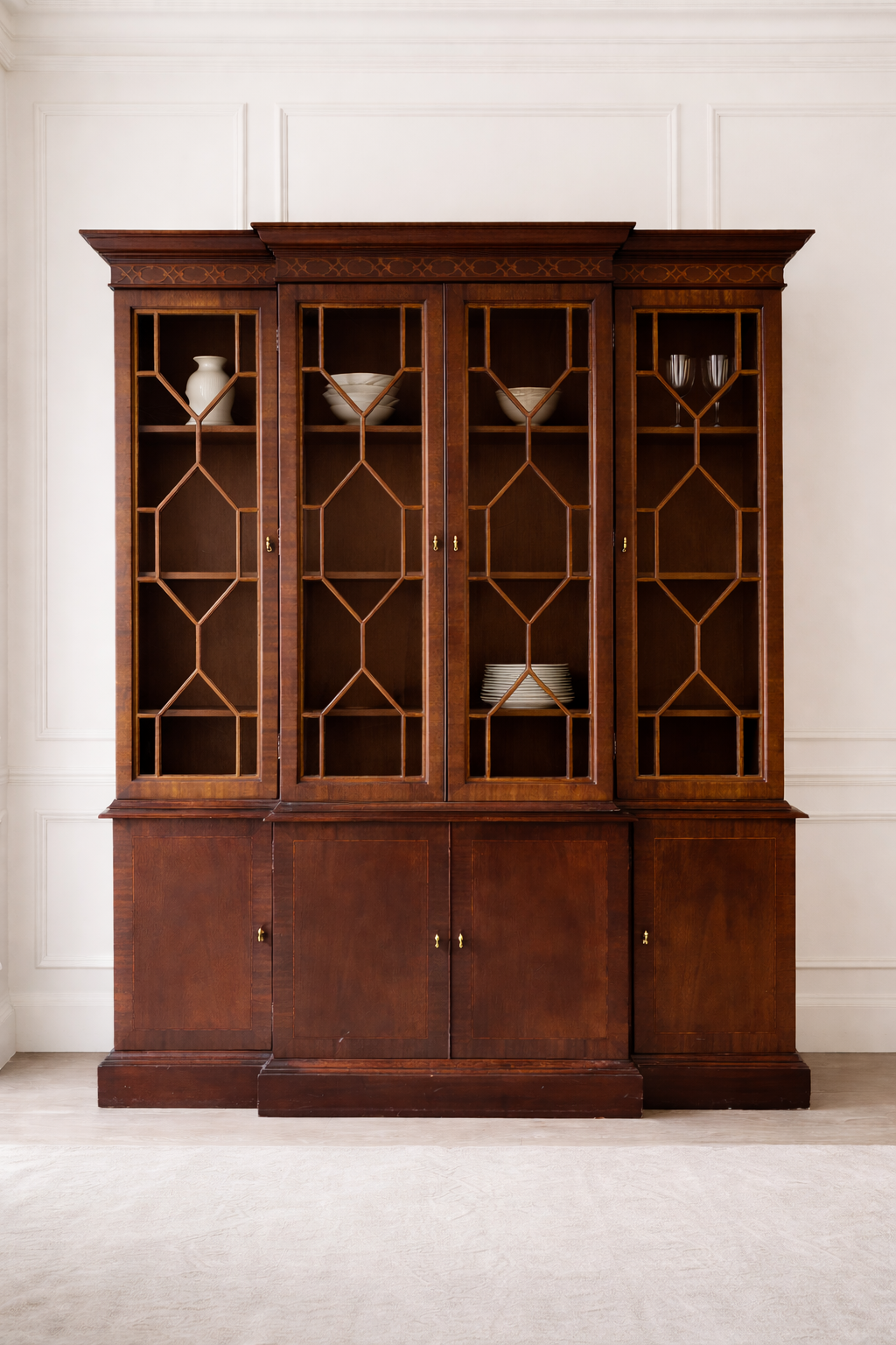 A tall wooden display cabinet with glass-paneled doors and decorative geometric patterns, holding a few ceramic and glassware items inside.