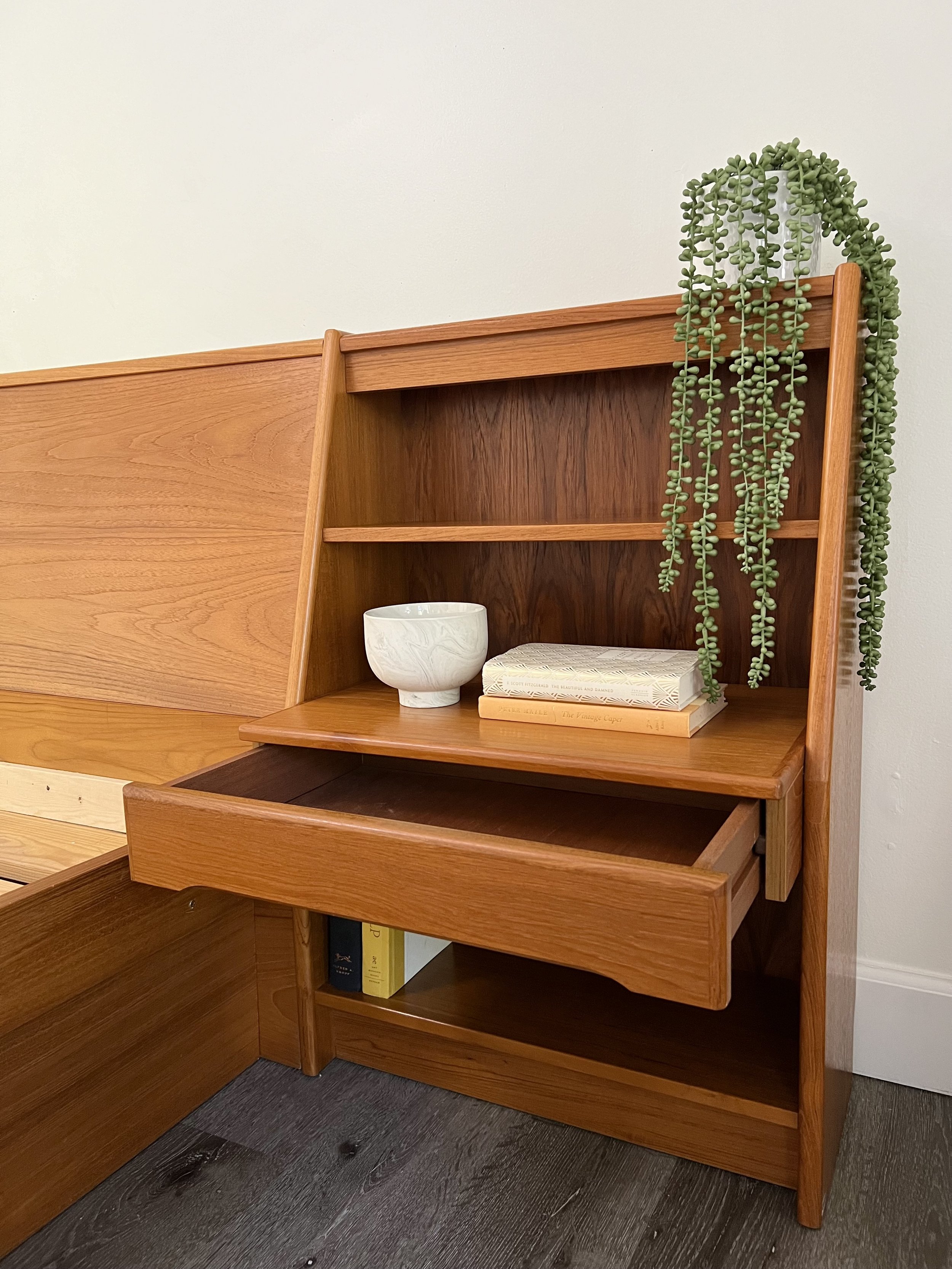 Wooden cabinet with open drawer, books, a white ceramic bowl, and a trailing green plant.