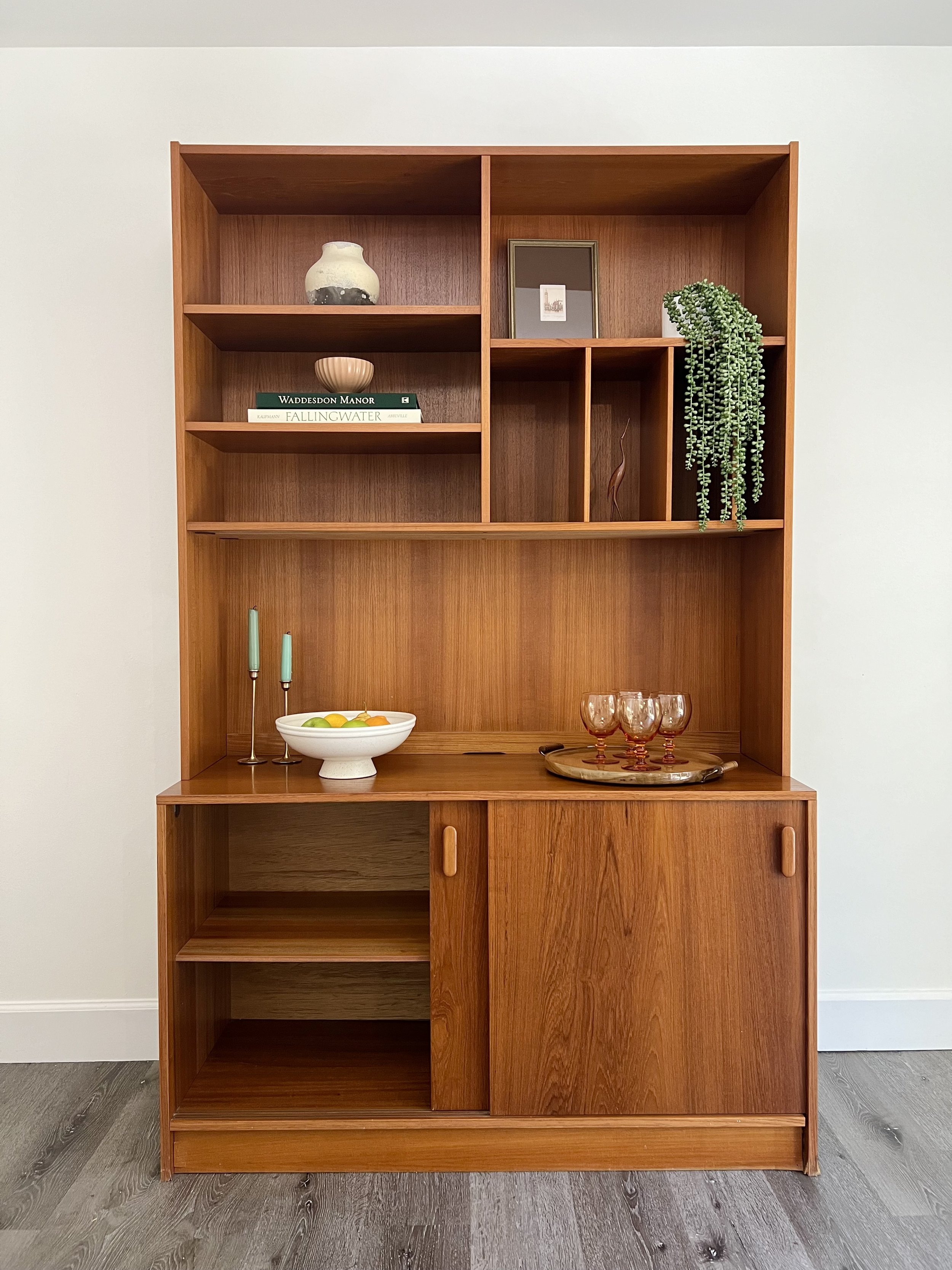 Wooden bookshelf with decorative items, books, and glassware arranged on the shelves.