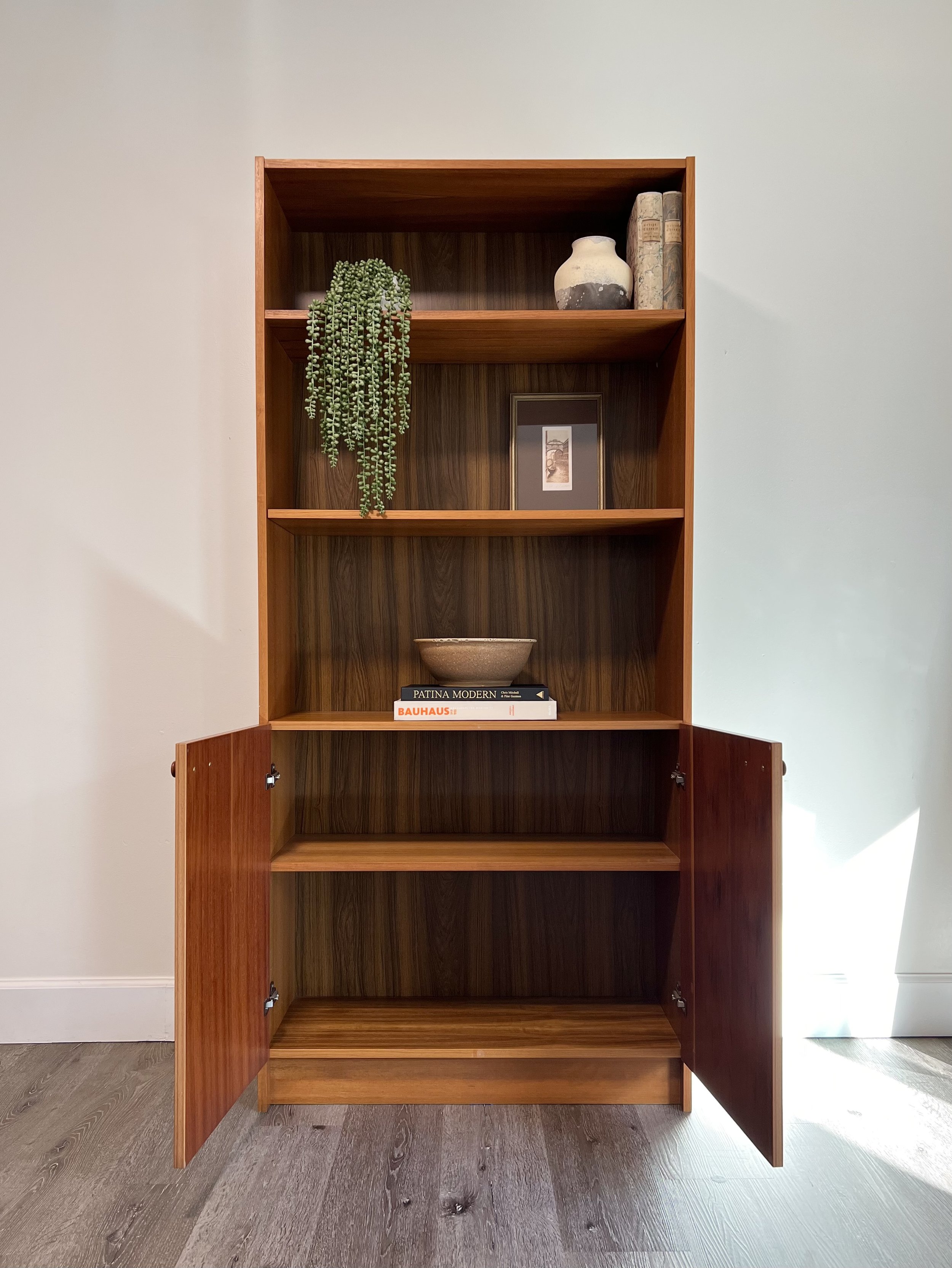 Empty wooden bookshelf with three shelves, some decor items, and a few books placed on the middle shelf.