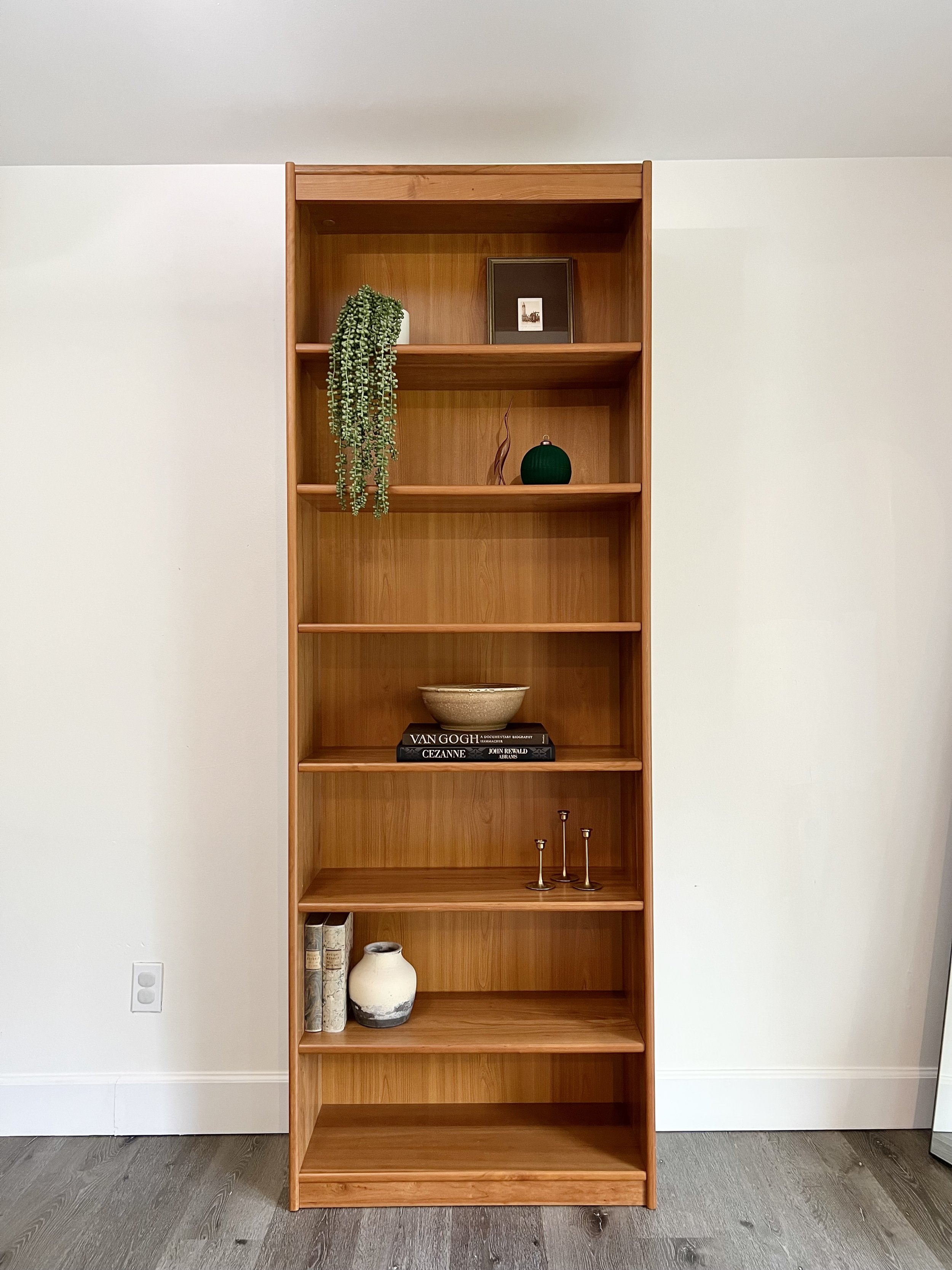 Empty wooden bookshelf with decorative items on a white wall.