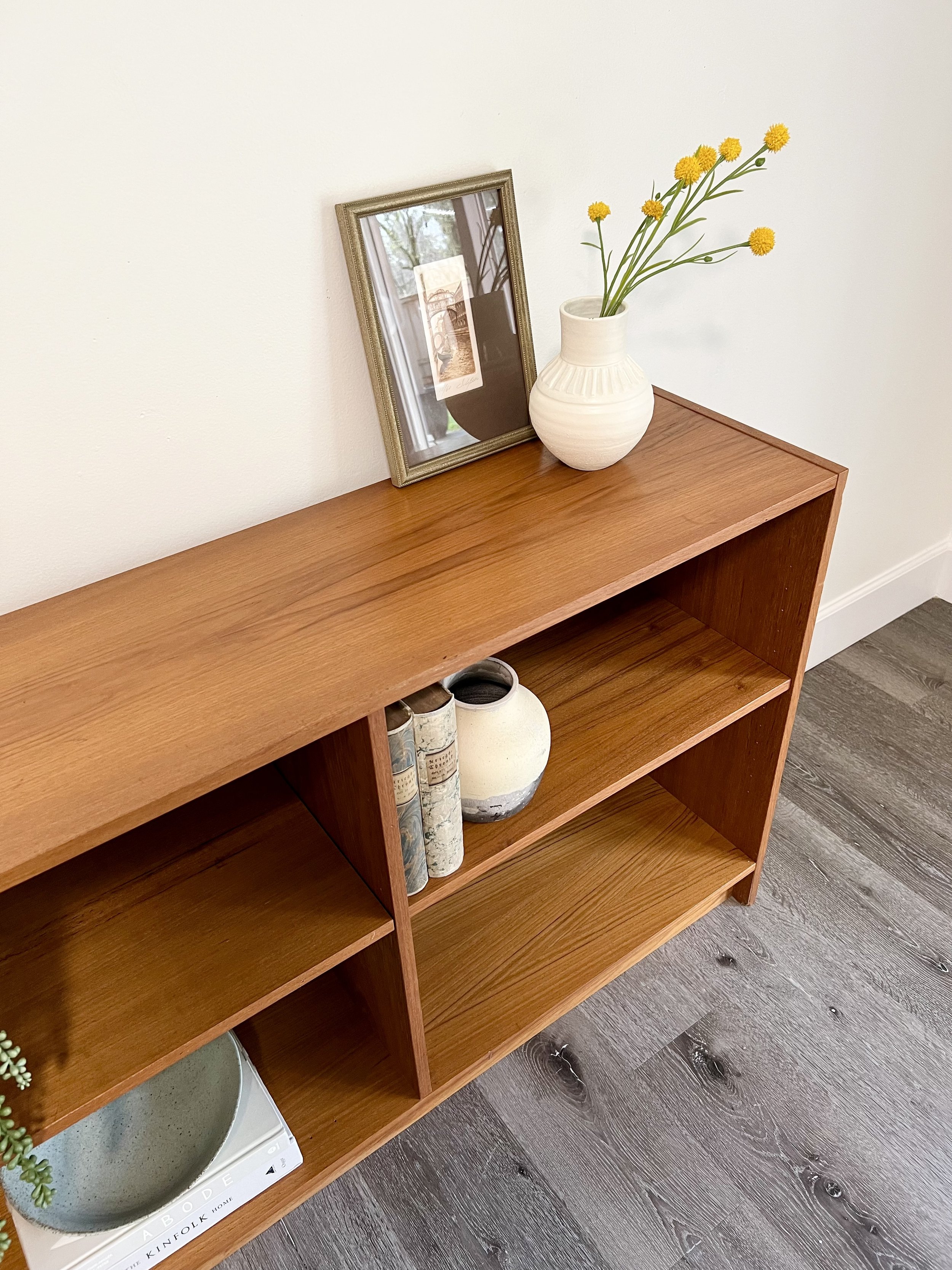 Wooden bookshelf with decorative vases, framed picture, and books, placed against a white wall.
