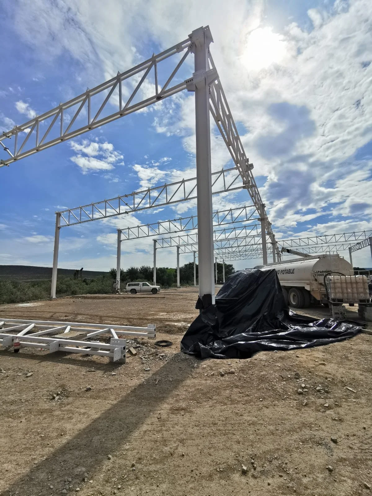 Estructuras metálicas blancas en construcción en un área al aire libre con cielo nublado, herramienta y maquinaria de construcción en el sitio.