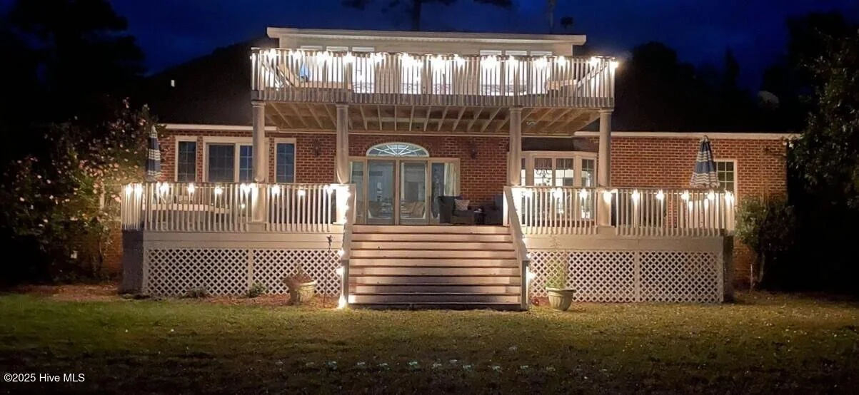 Back of a brick house with two-story deck decorated with string lights at night.