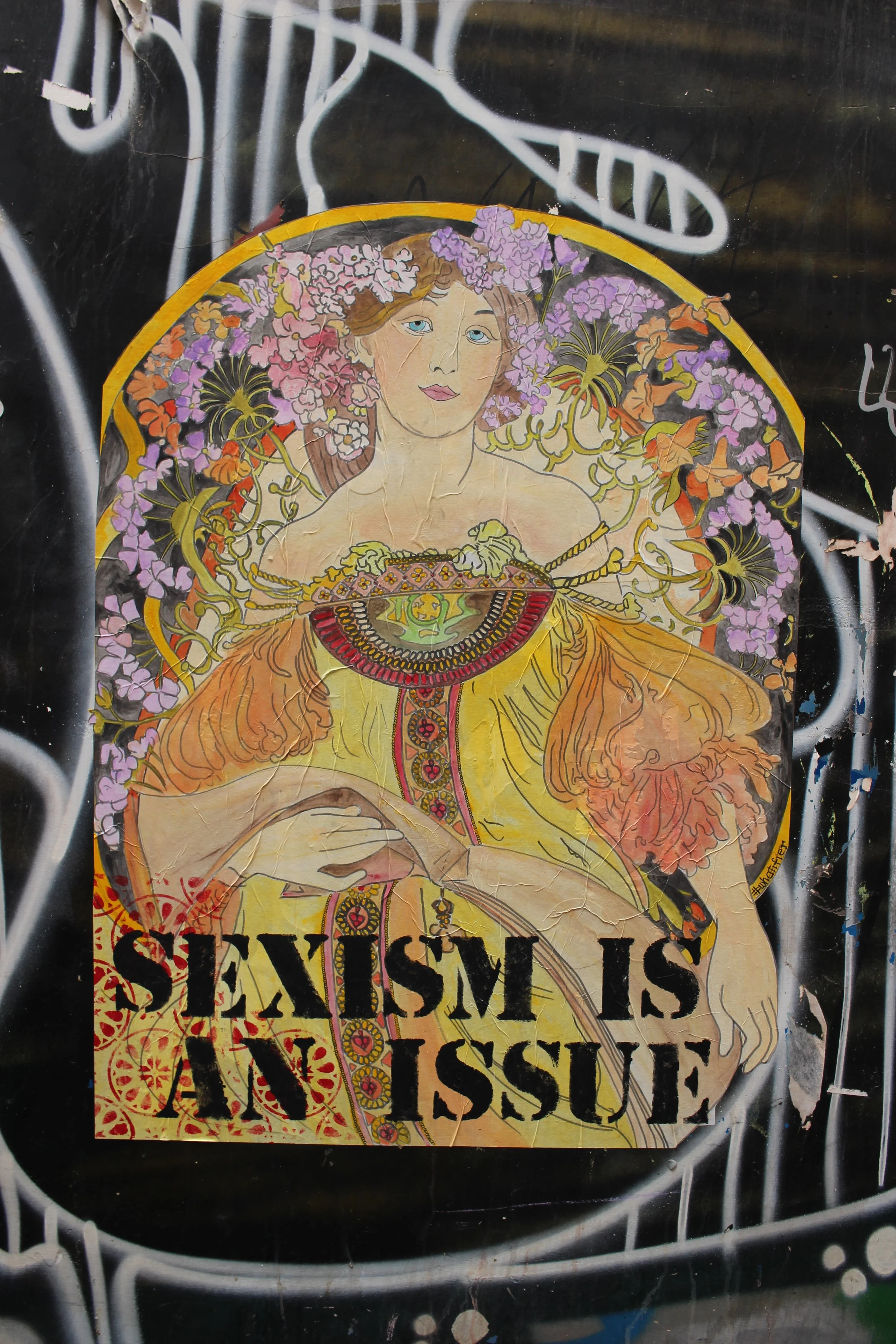 Grafische Illustration einer Frau mit Blumen im Haar, in einem bunten hebräischen Kleid, mit dem Text „SEXISM IS AN ISSUE“ darunter.