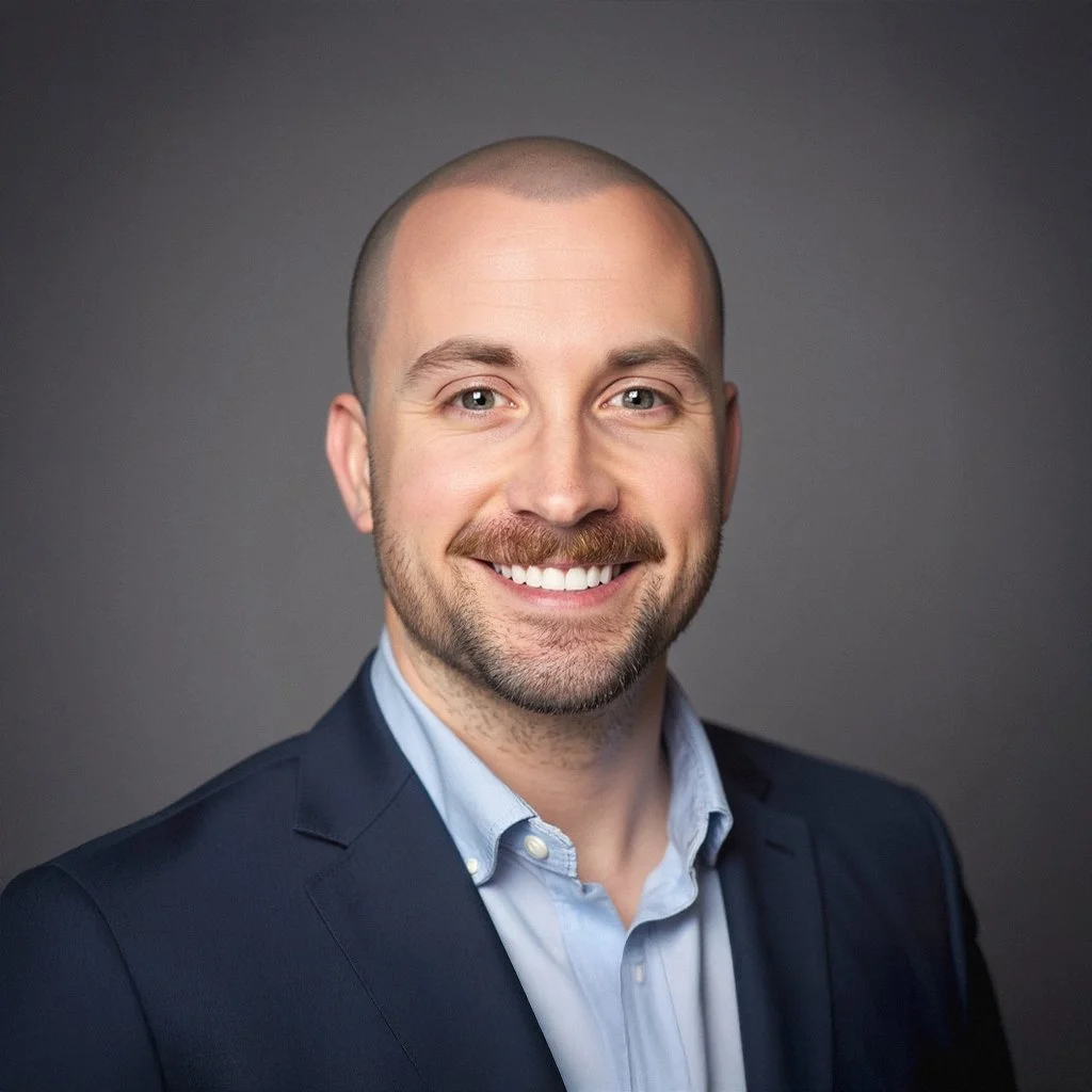 Professional headshot of a smiling man with a beard, wearing a navy blazer and light blue shirt, against a gray background.