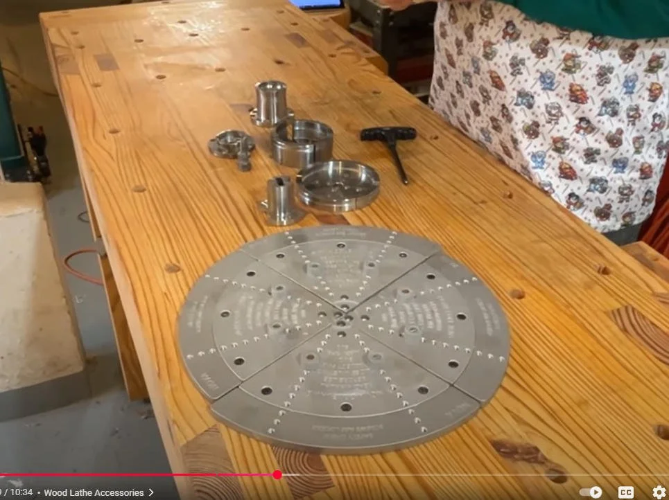 A wooden workbench with metal lathe accessories, a metal circle, and a T-handle wrench on top.