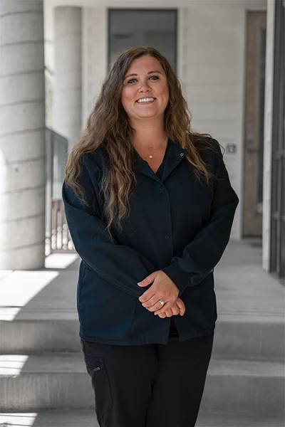 A woman with long, curly hair smiling on a building porch.