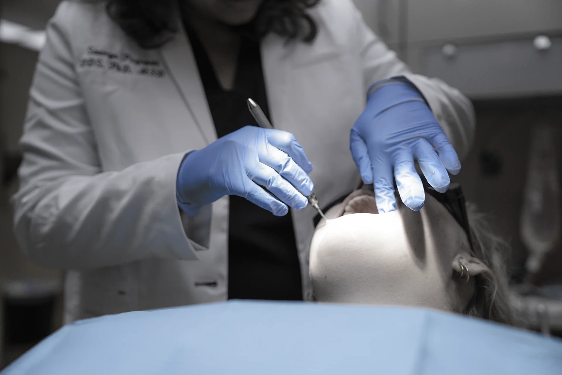 Medical professional administering anesthesia to a patient during a medical procedure, wearing blue gloves and a white coat.