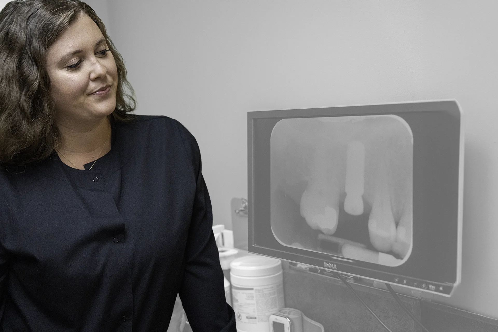 A woman wearing a black shirt looking at a computer monitor in a medical or clinical setting.