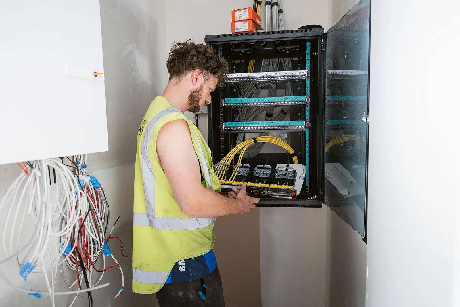 Electrician working on a server rack with yellow cables, wearing a yellow safety vest.