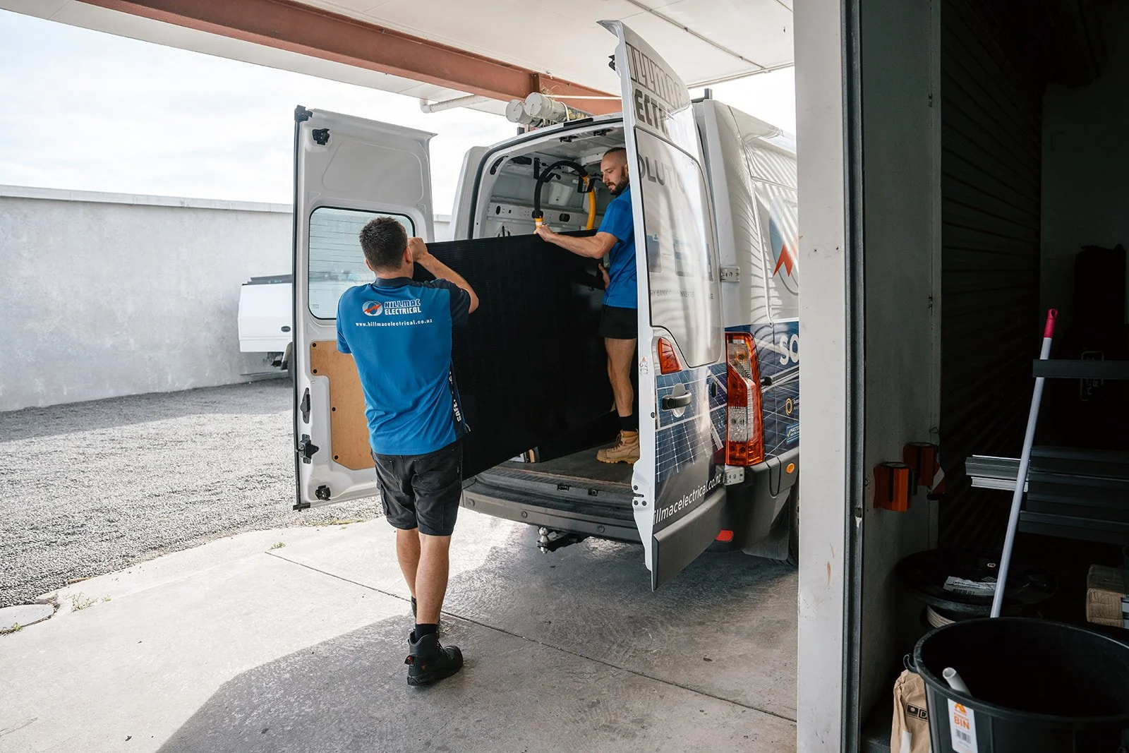 Two workers unloading a large black electronic item from a service van.