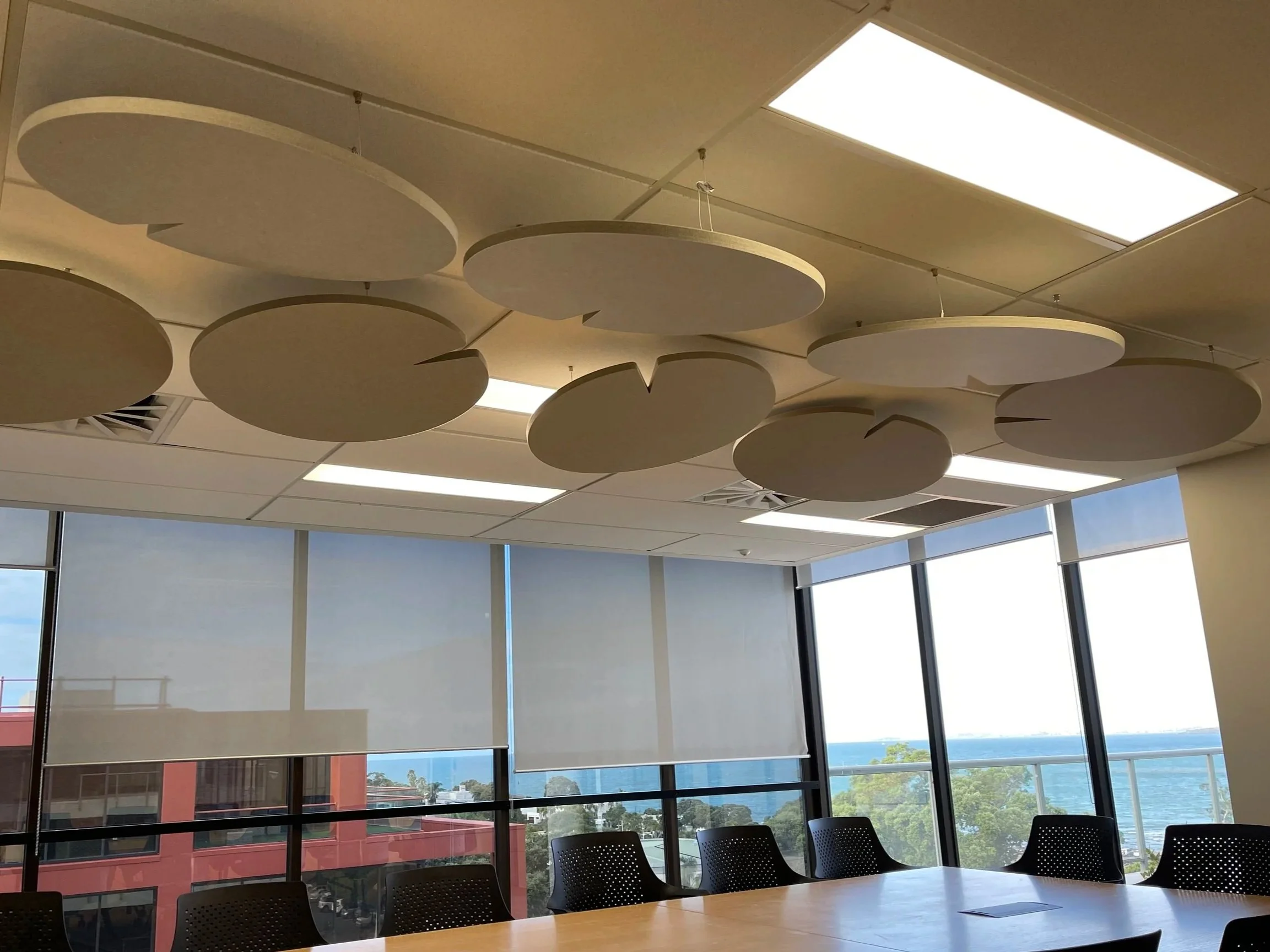 Conference room with large windows showing an ocean view, black chairs, and decorative ceiling panels.