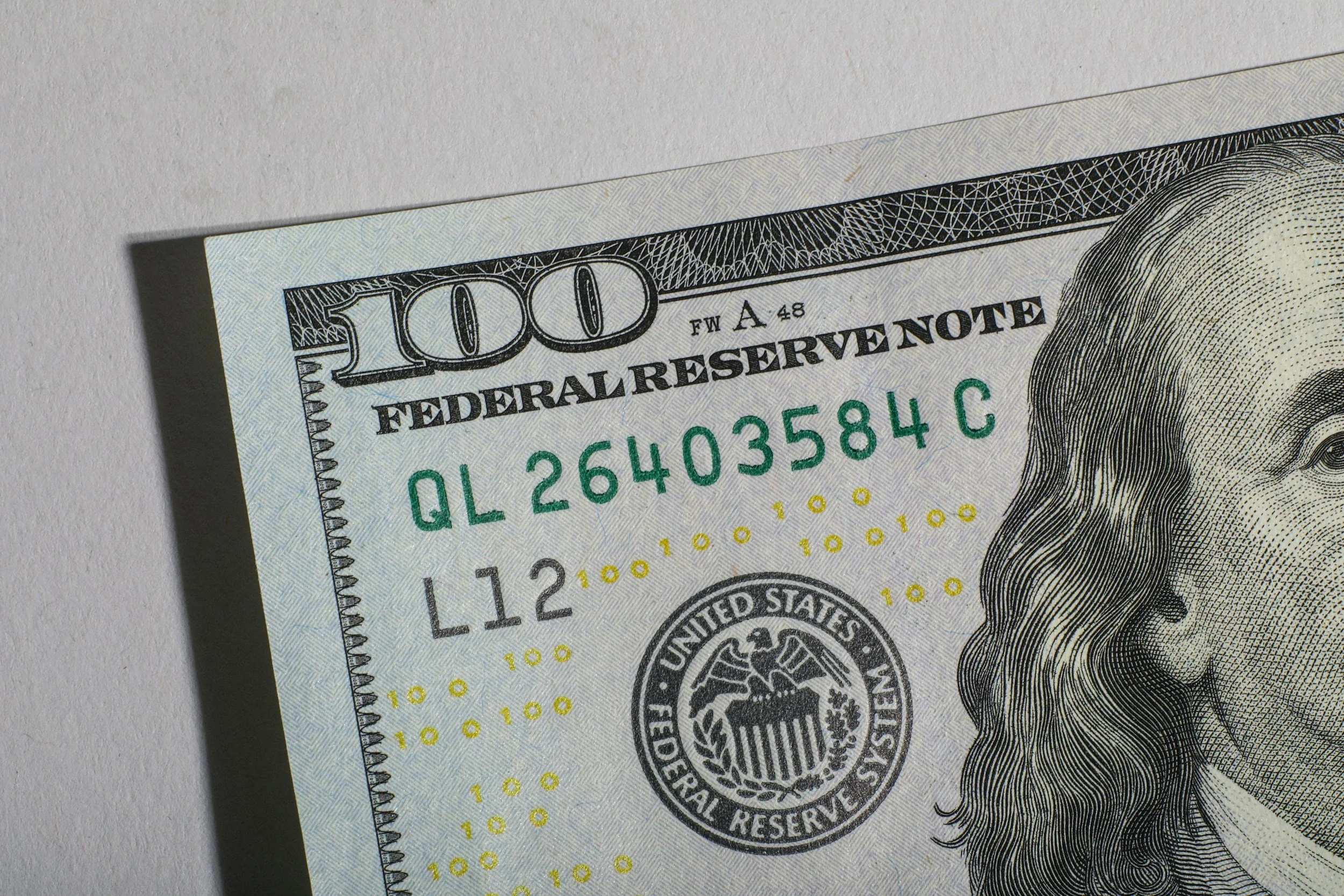 Close-up of a $100 US dollar bill, showing the top left corner, part of Benjamin Franklin's portrait, and the Federal Reserve note seal.