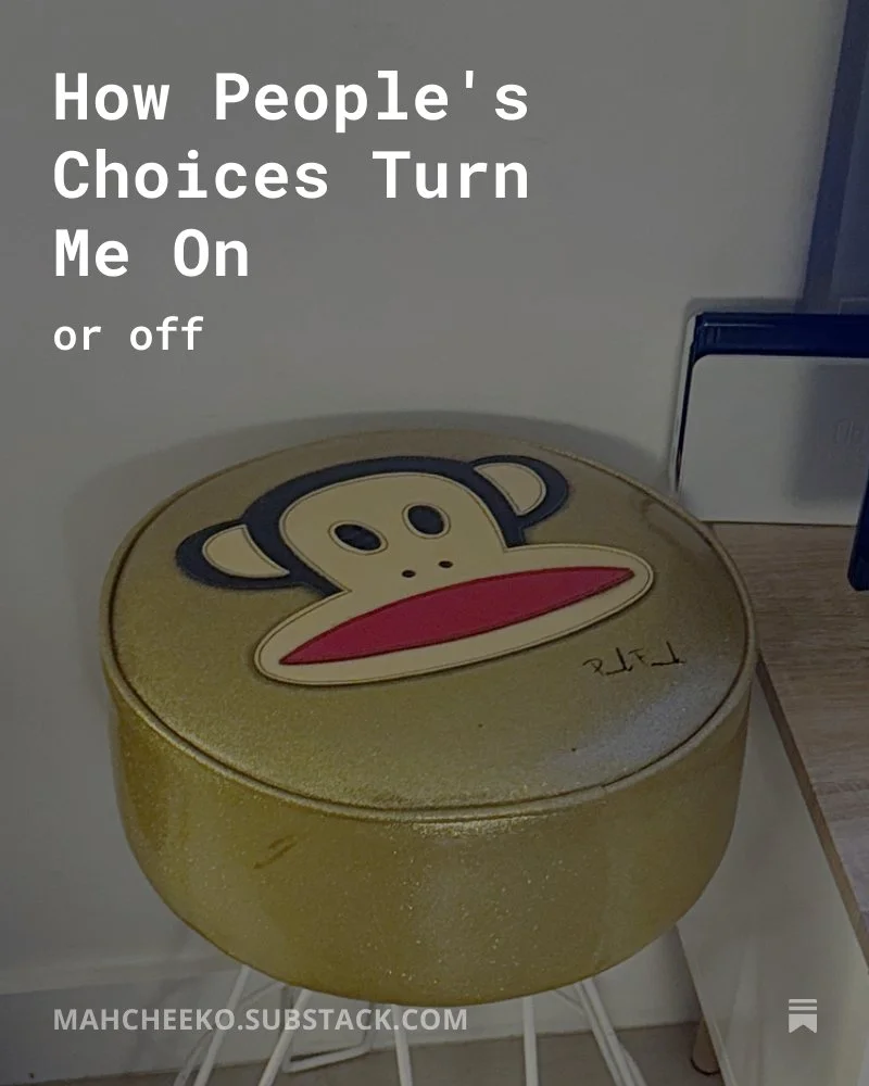 A round, golden-yellow container with a monkey face on the top, featuring large eyes, ears, and a red mouth, placed on a white stand in a room with a white wall and a wooden surface with a box or device nearby.