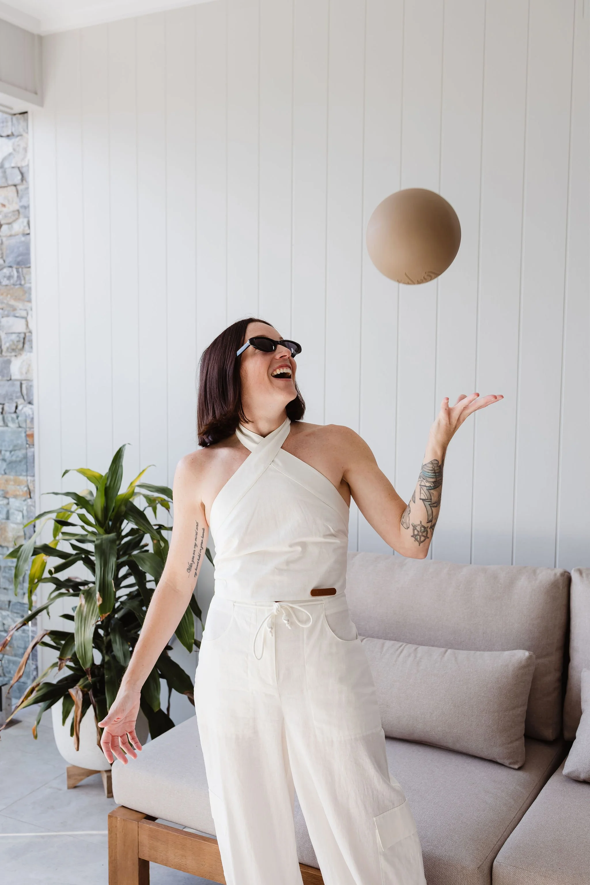Studio em. Academy founder and Pilates educator Em smiling while tossing a Pilates ball, wearing a white linen outfit in a bright, contemporary studio.
