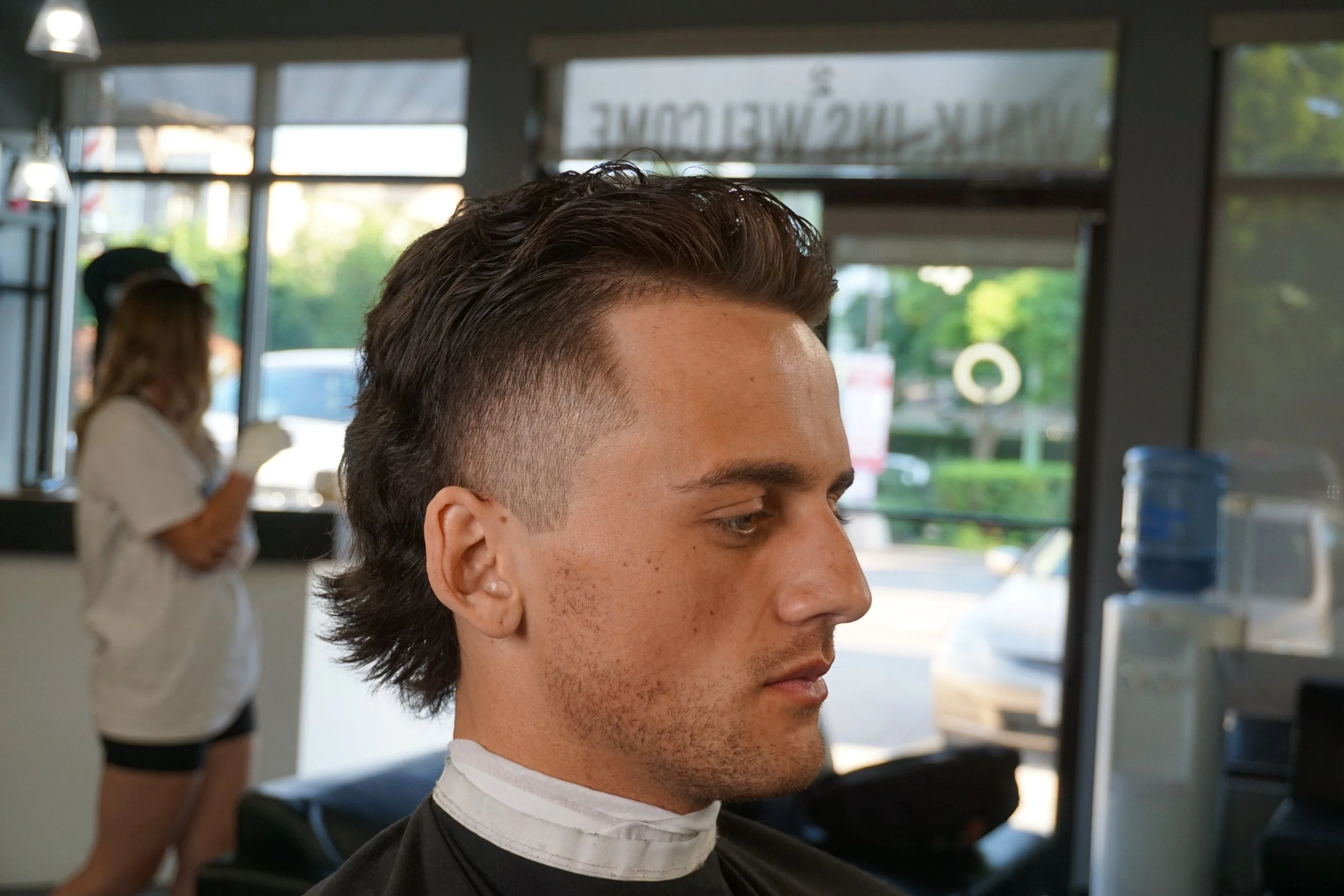 Young man getting a haircut in a salon with a barber wearing a white apron.