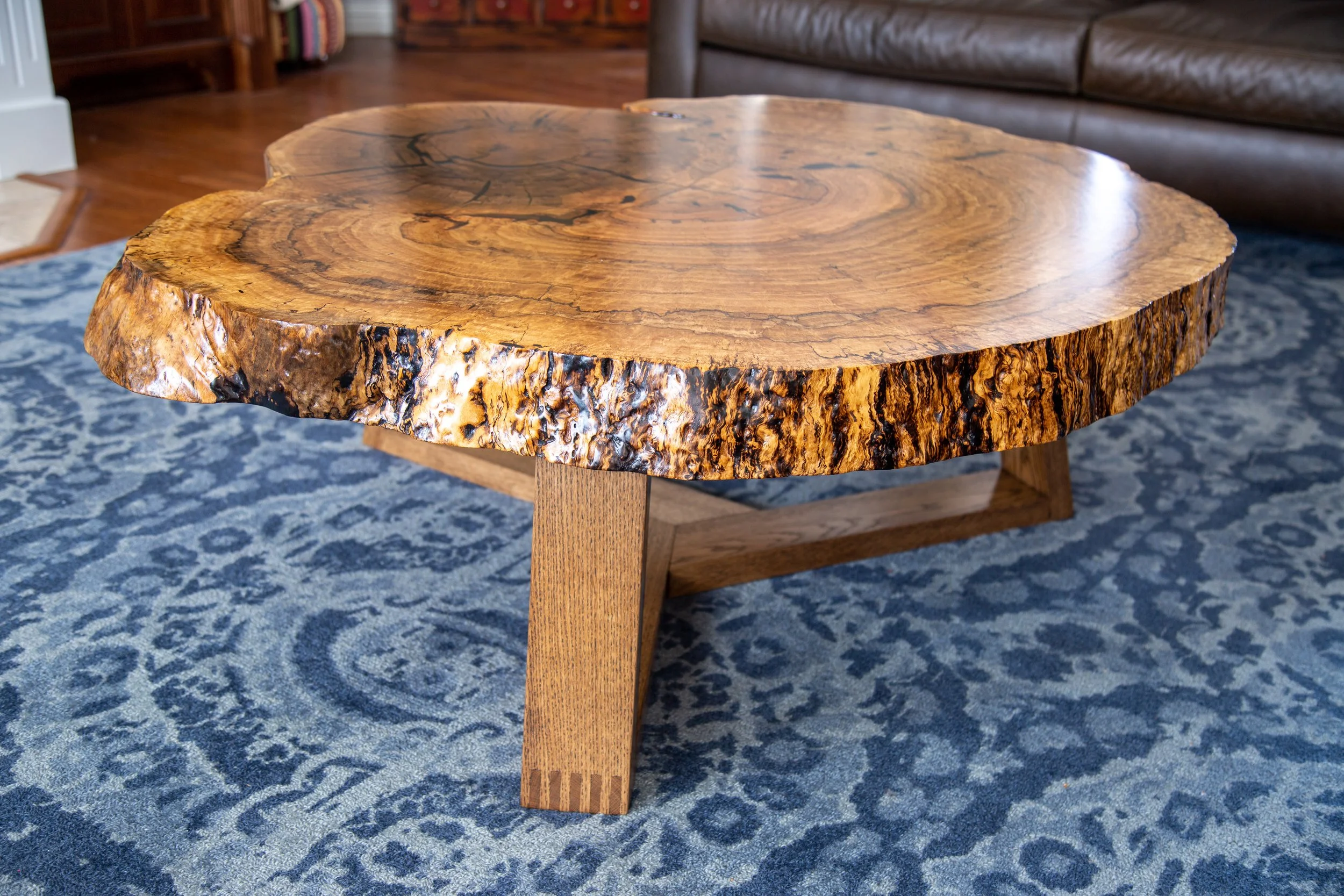 200-year old White Oak Burl coffee table, made from a single slab of natural wood with a live edge, placed on a patterned blue and white rug in a living room.
