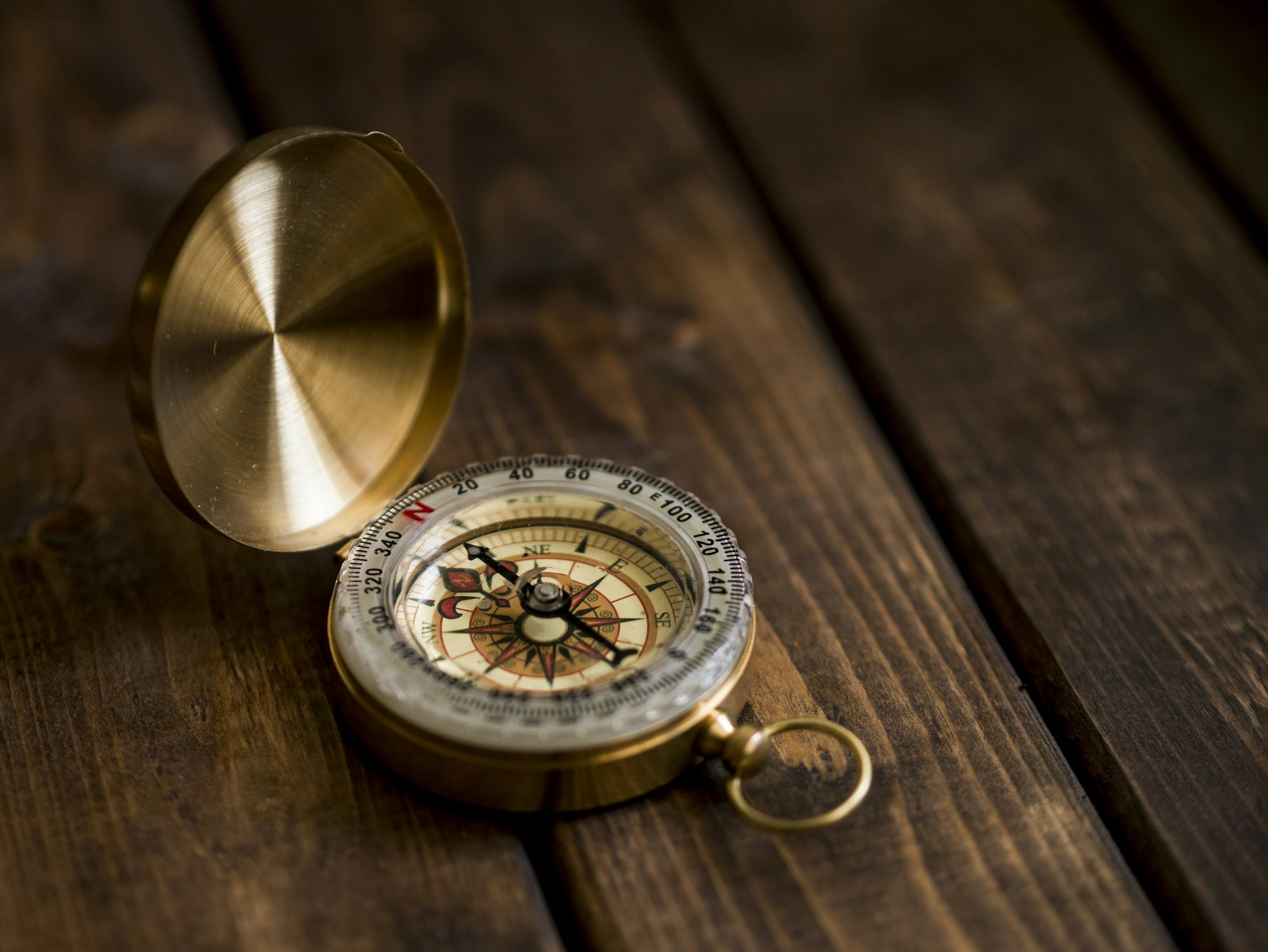 A vintage brass compass with a lid open, resting on a wooden surface.