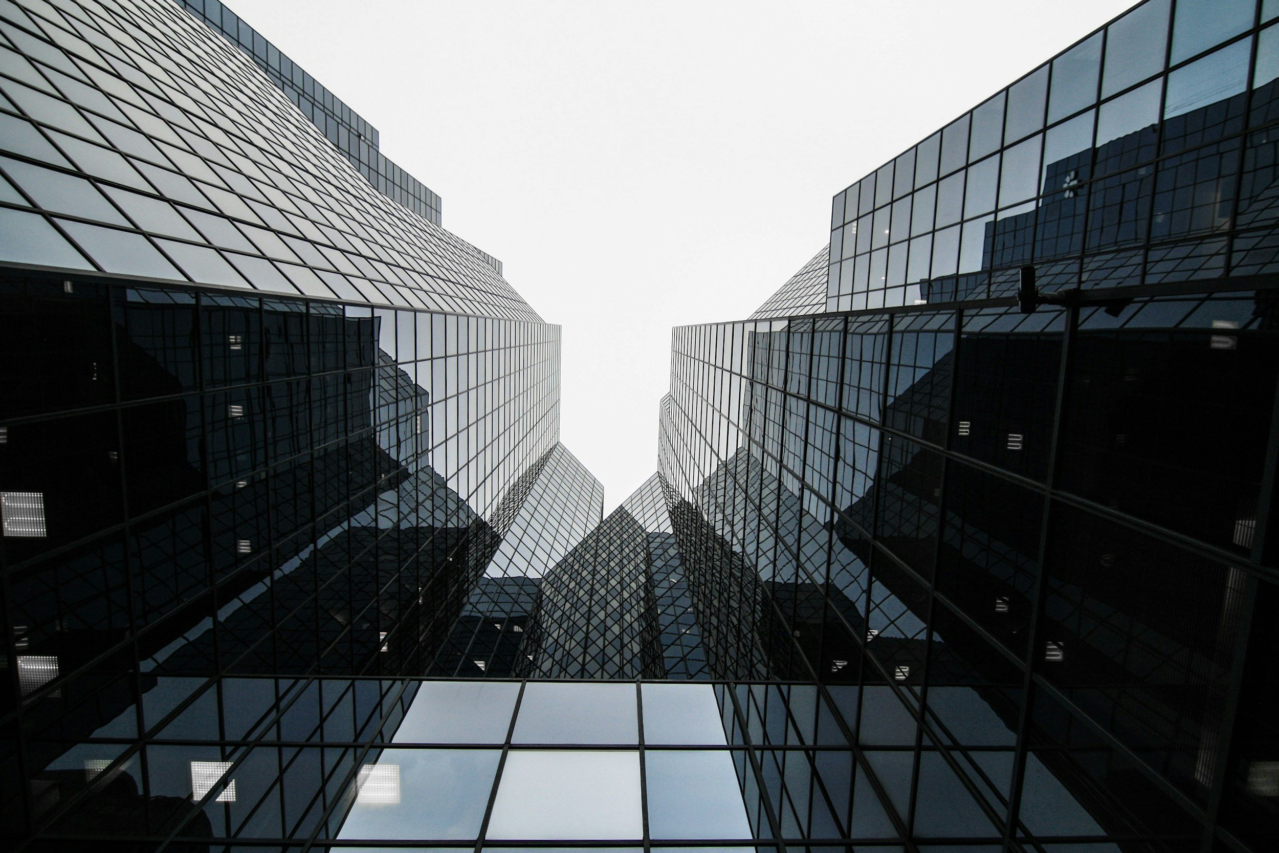 View of modern glass office buildings from below, showing reflective windows and sharp architectural lines against a white sky.