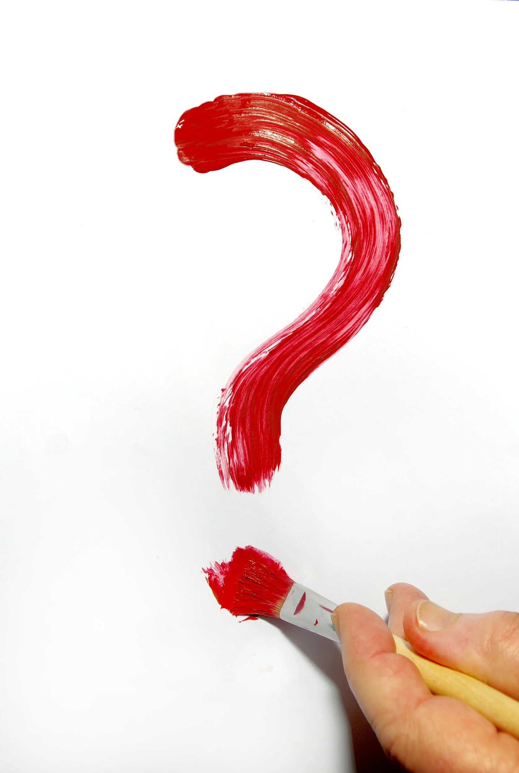 A hand holding a paintbrush paints a red question mark on a white surface.