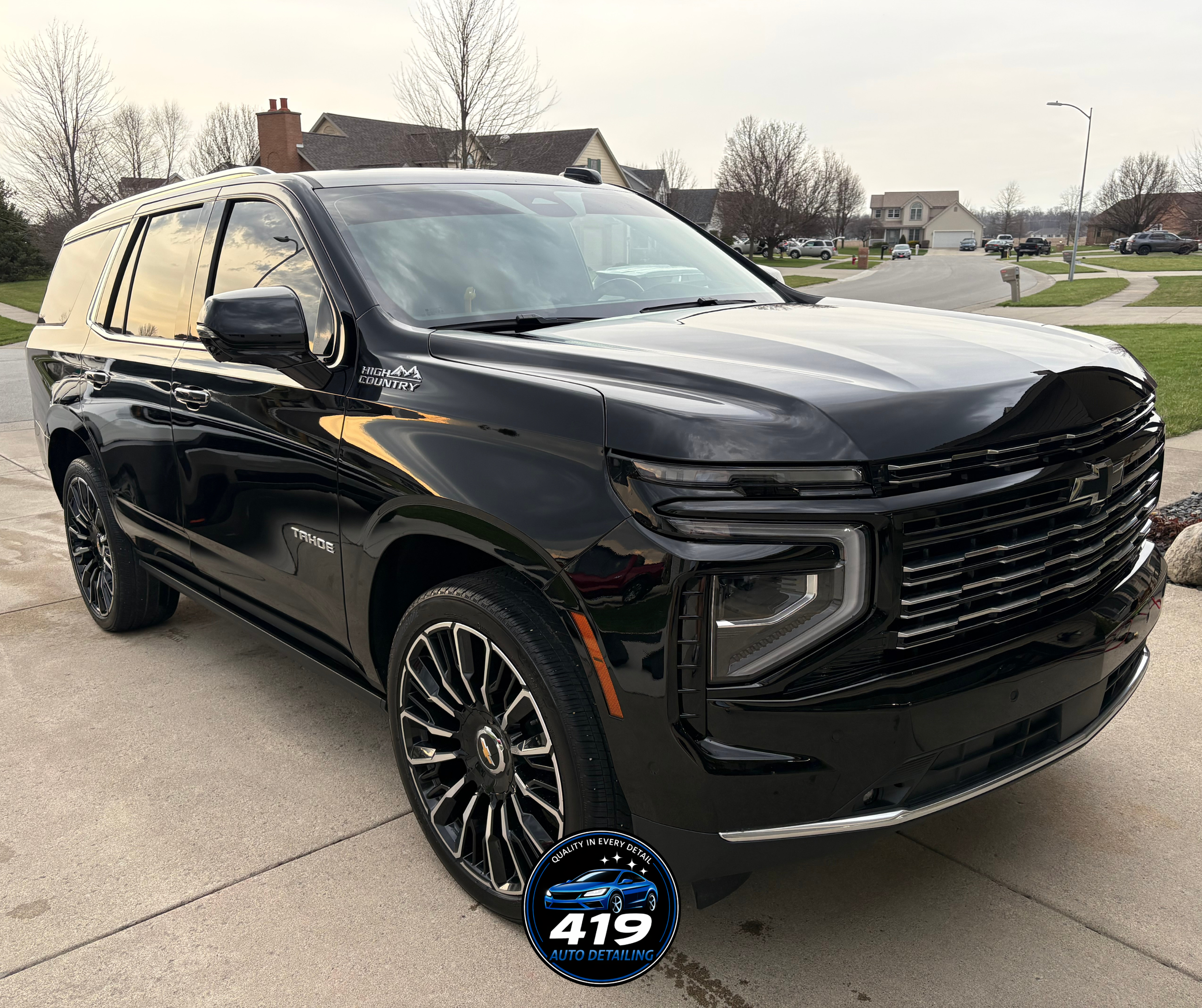 A black Chevrolet Tahoe SUV parked on a concrete driveway in a suburban neighborhood during daytime with houses and trees in the background.
