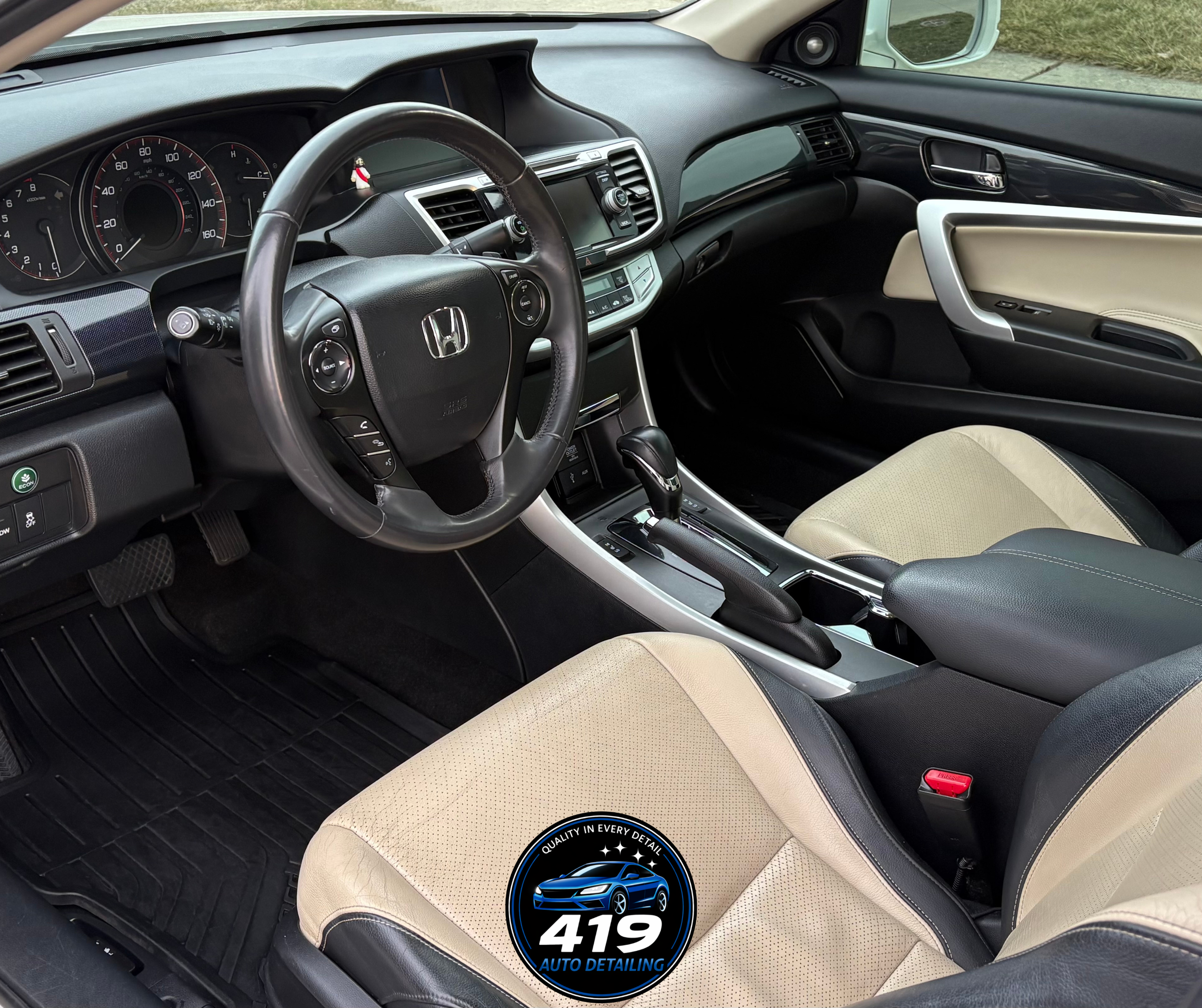 Interior view of a Honda car with beige and black seats, a black steering wheel, dashboard, and gear shift, with a logo for 419 Auto Detailing on the passenger seat.