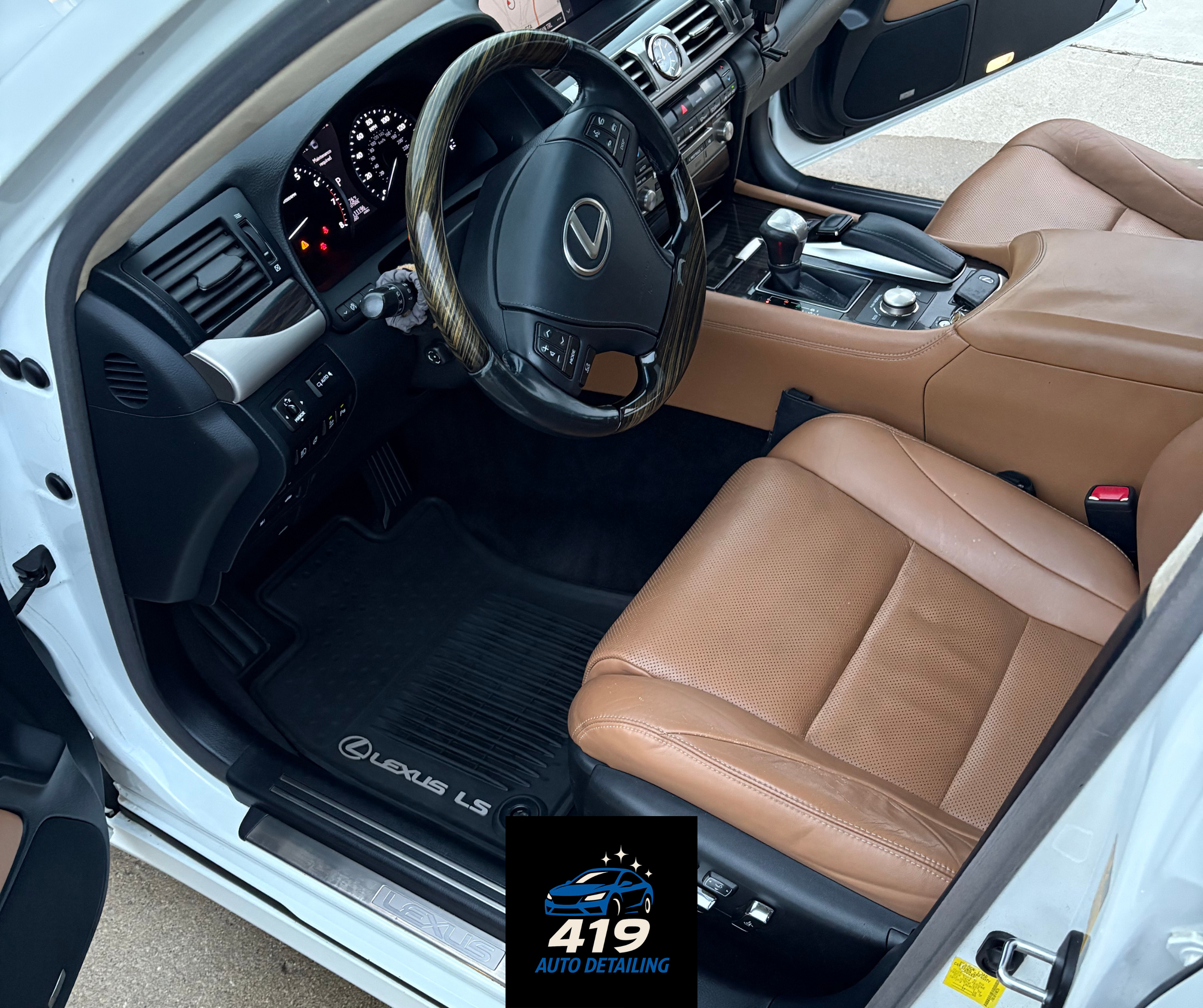 Interior of a Lexus LS with tan leather seats, a black steering wheel, and a black dashboard with various controls. The floor has a black Lexus-branded floor mat, and there is a black auto detailing logo with a blue car and the text '419 Auto Detaili