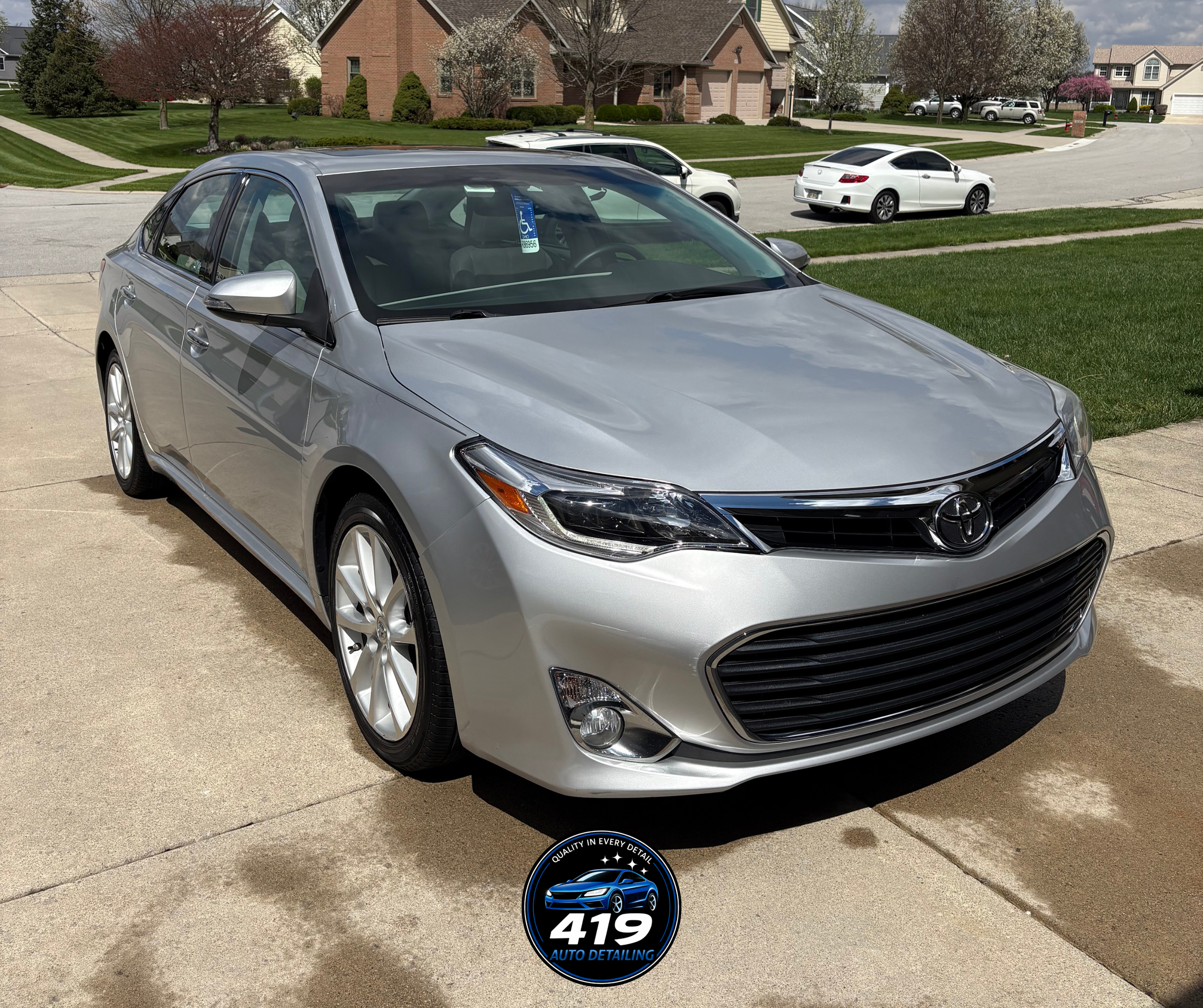 Silver Toyota sedan parked on a driveway in a suburban neighborhood with houses and trees in the background.