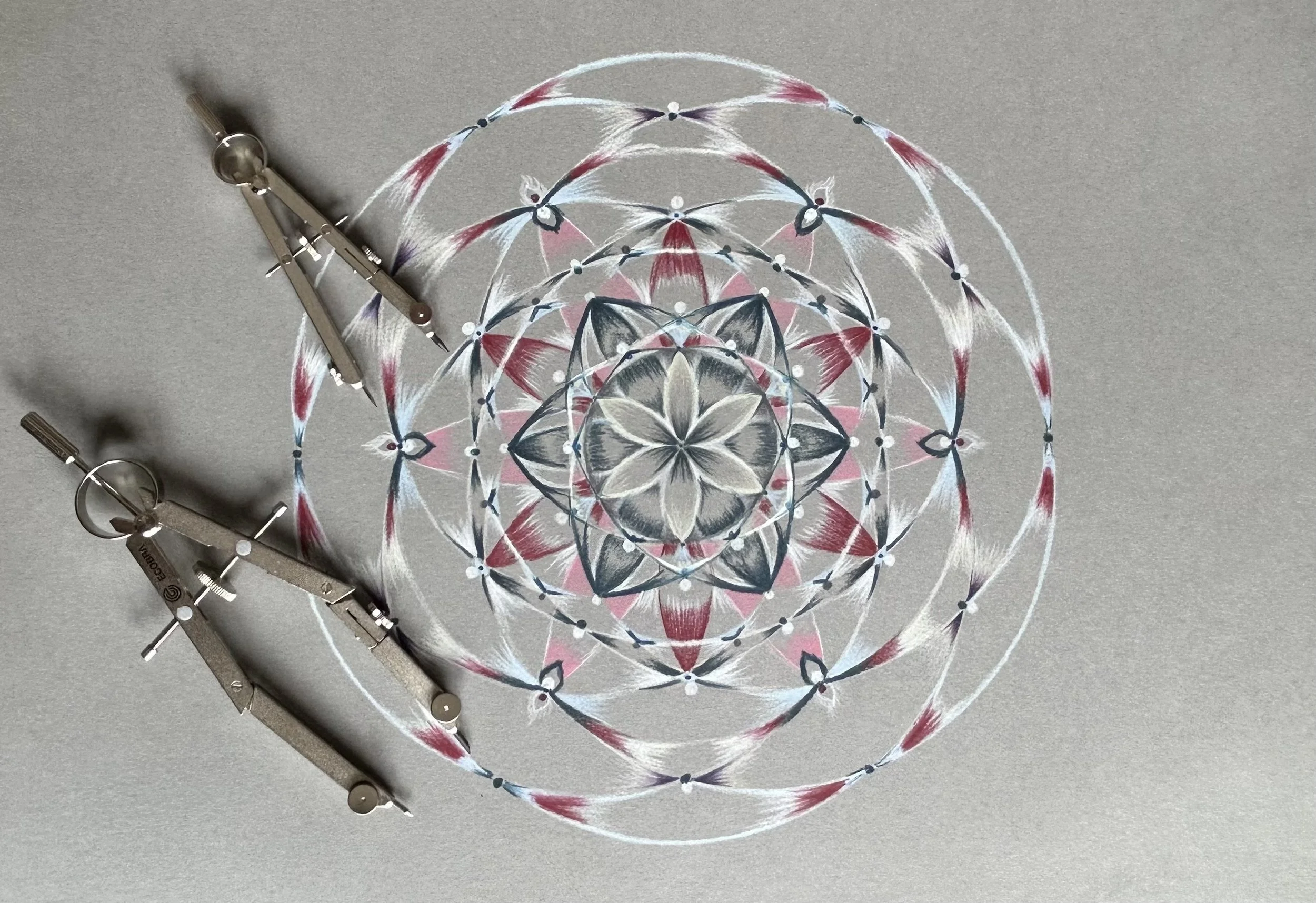 Ein geometrisches Mandala aus farbigen Federn und Mustern, daneben ein Zirkel zum Zeichnen.