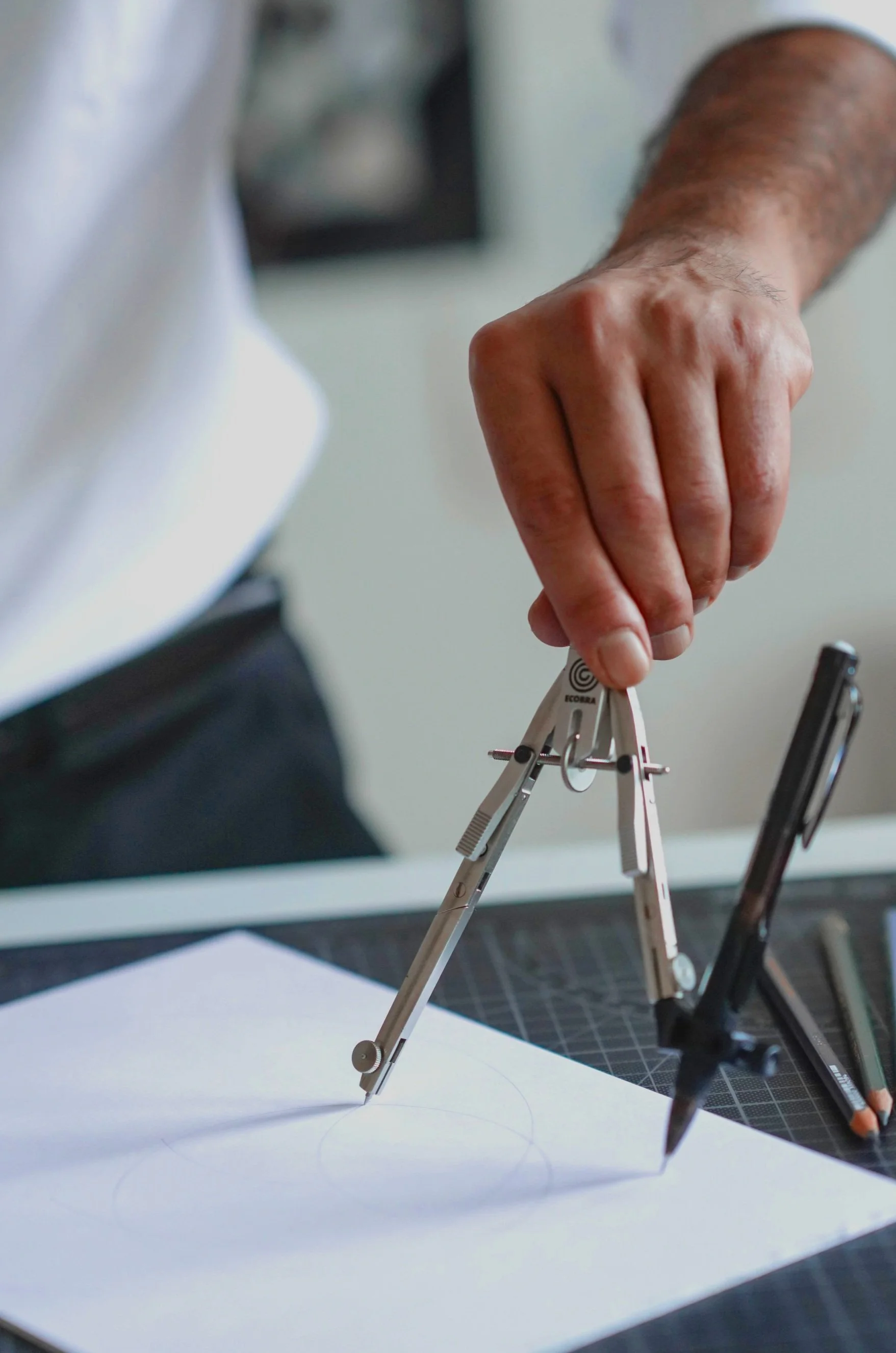 Hand eines Architekten oder Ingenieurs, der mit einem Zirkel auf einem technischen Zeichenblatt zeichnet.