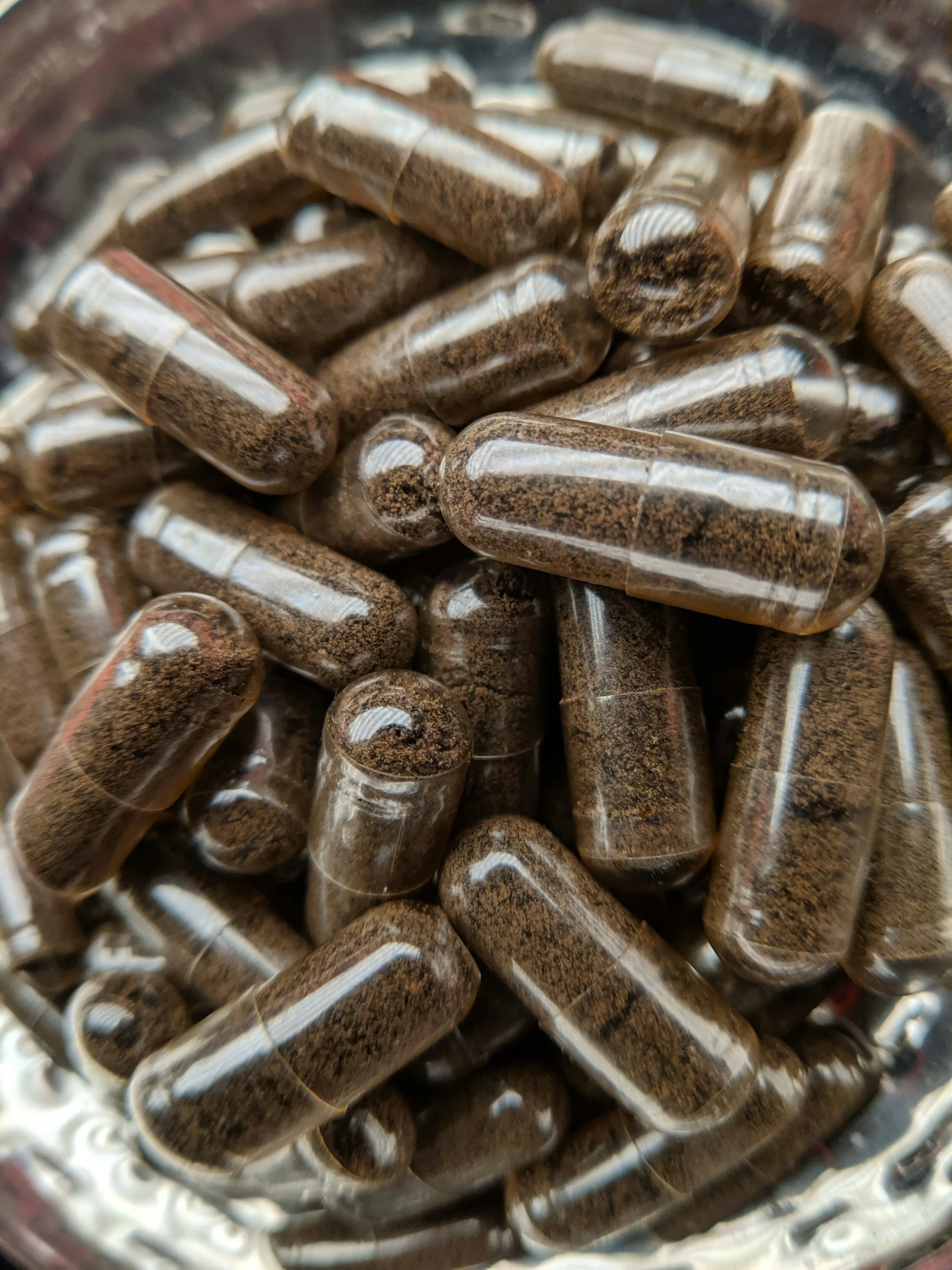 Close-up view of capsules filled with dried herbs or powder, inside a glass container or jar.