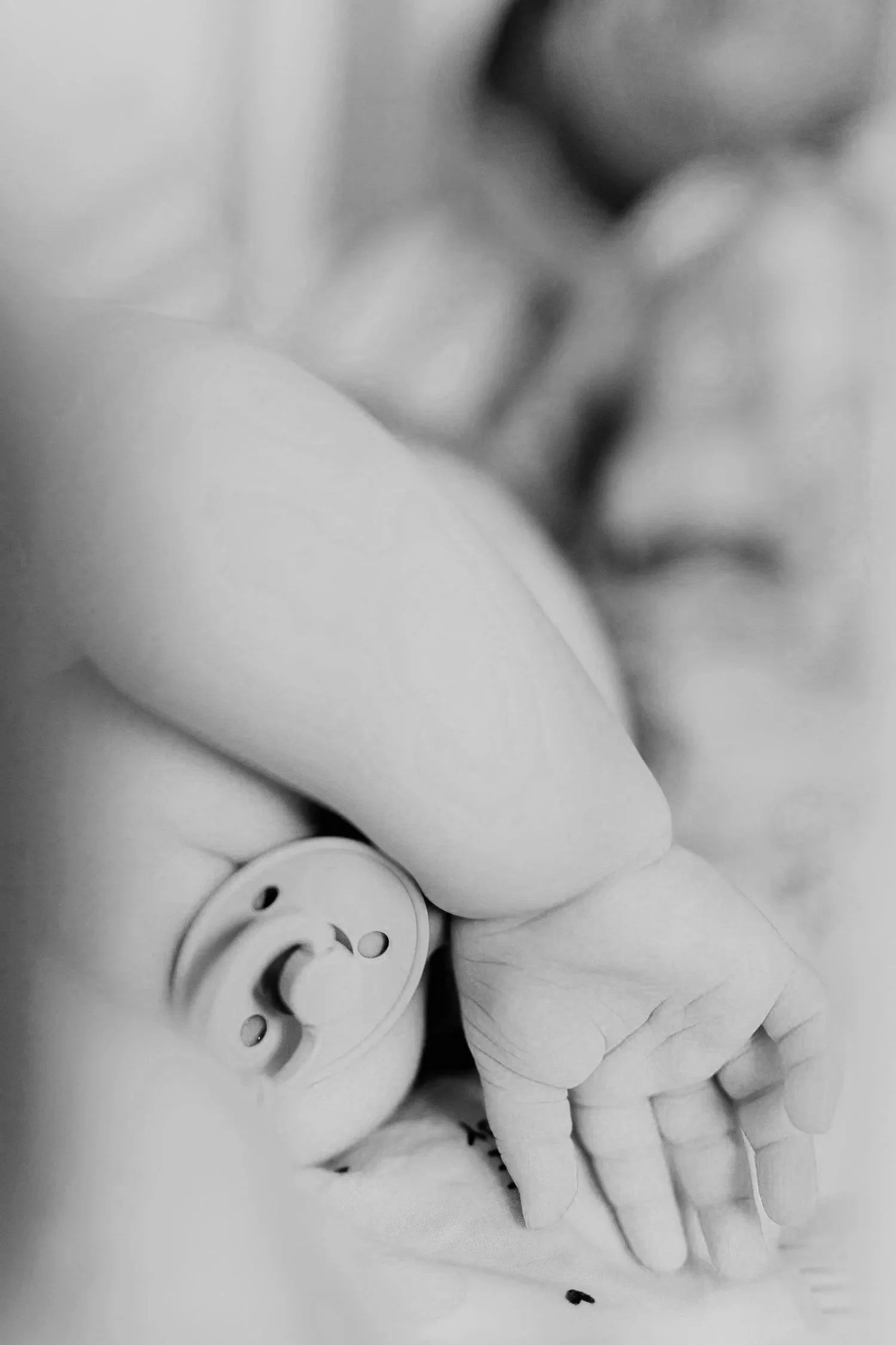 Close-up black and white photo of a person's hand holding a pacifier, with baby pacifiers placed nearby.