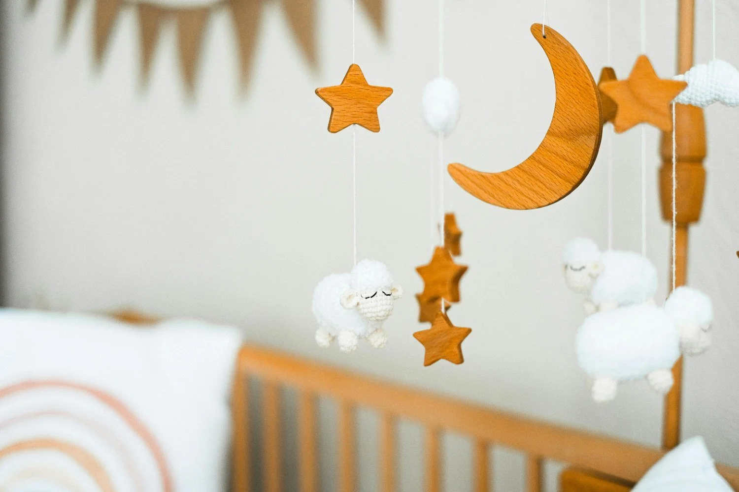 Wooden mobile featuring a crescent moon, stars, and fluffy sheep hanging in a nursery.