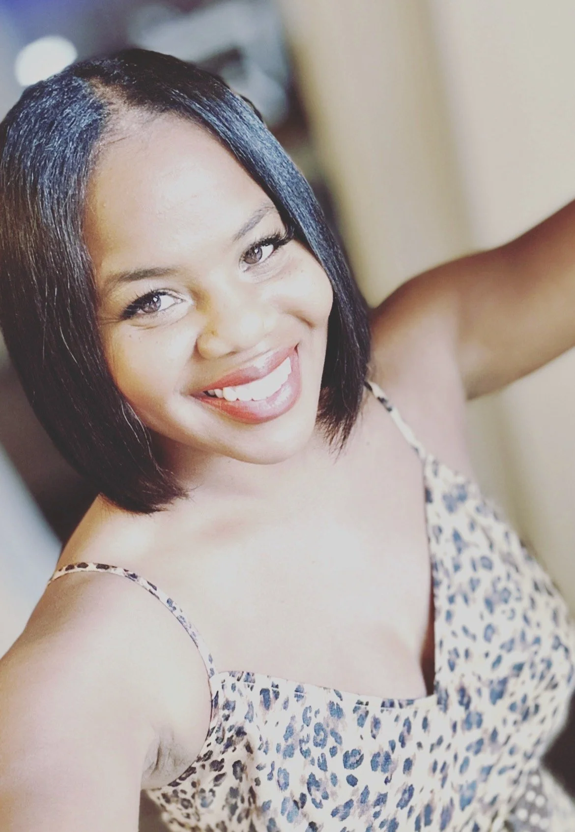 Close-up of a woman with shoulder-length black hair, smiling and wearing a leopard-print sleeveless top.