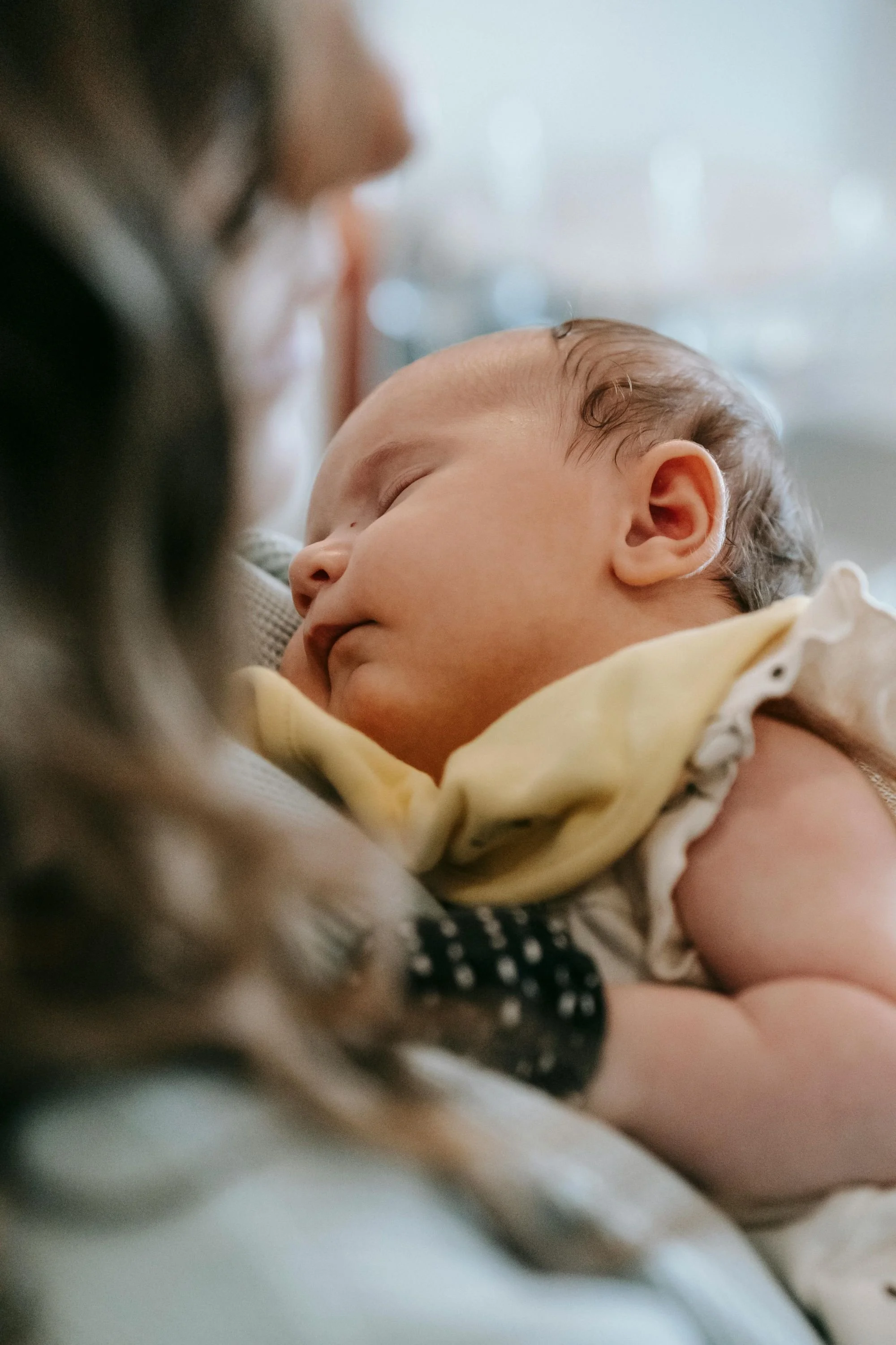 A close-up of a sleeping baby with closed eyes, held gently by an adult.