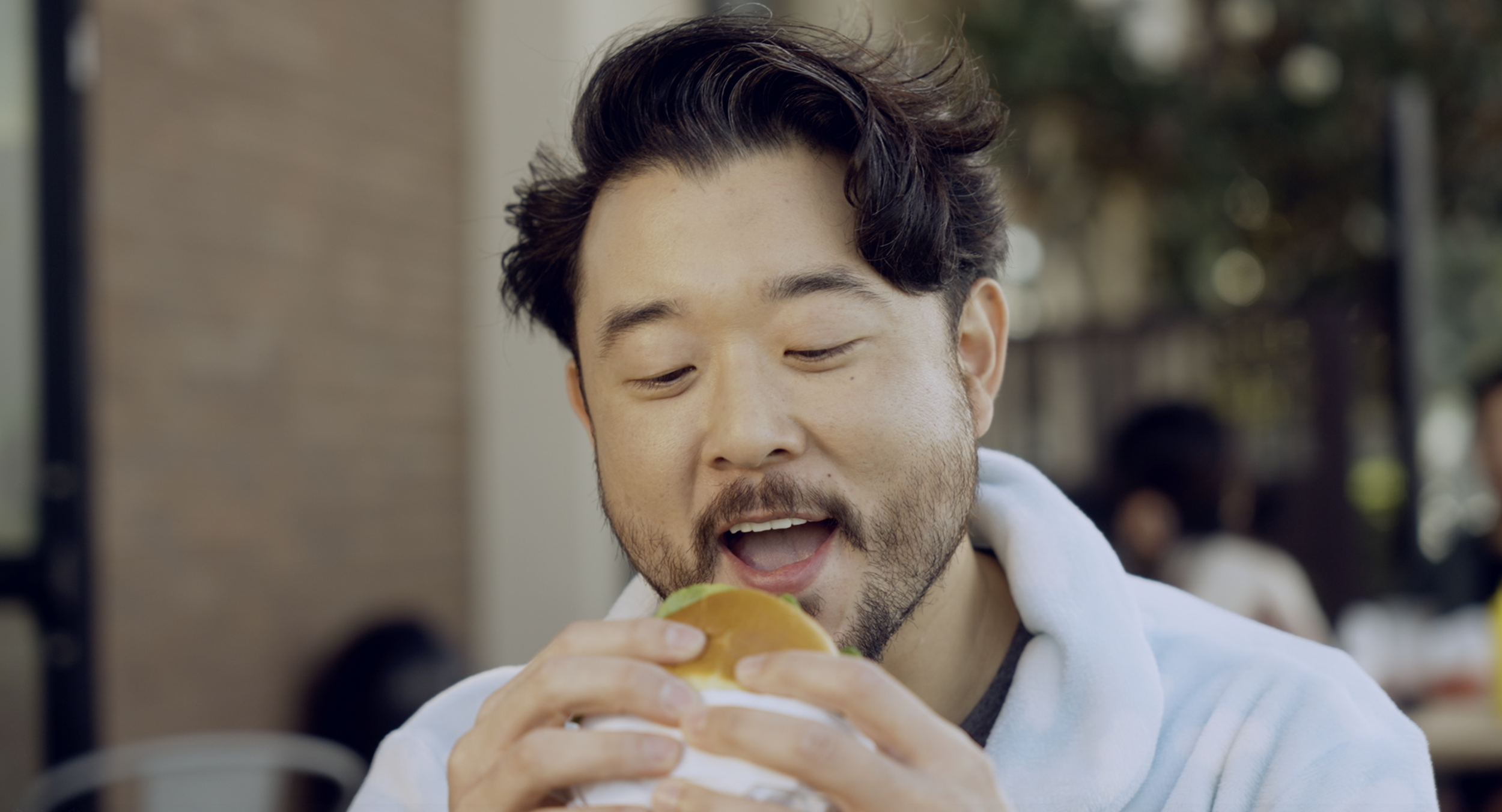 A man about to take a bite of a burger at an outdoor setting.