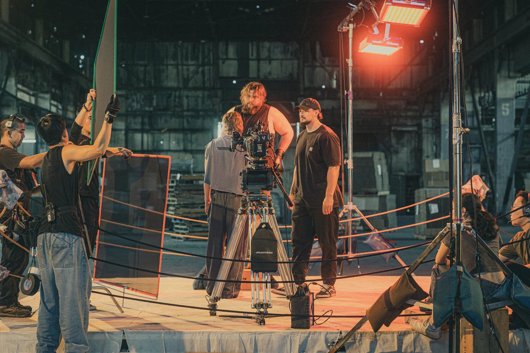 Film crew working on a set with camera equipment and lighting in an industrial warehouse.