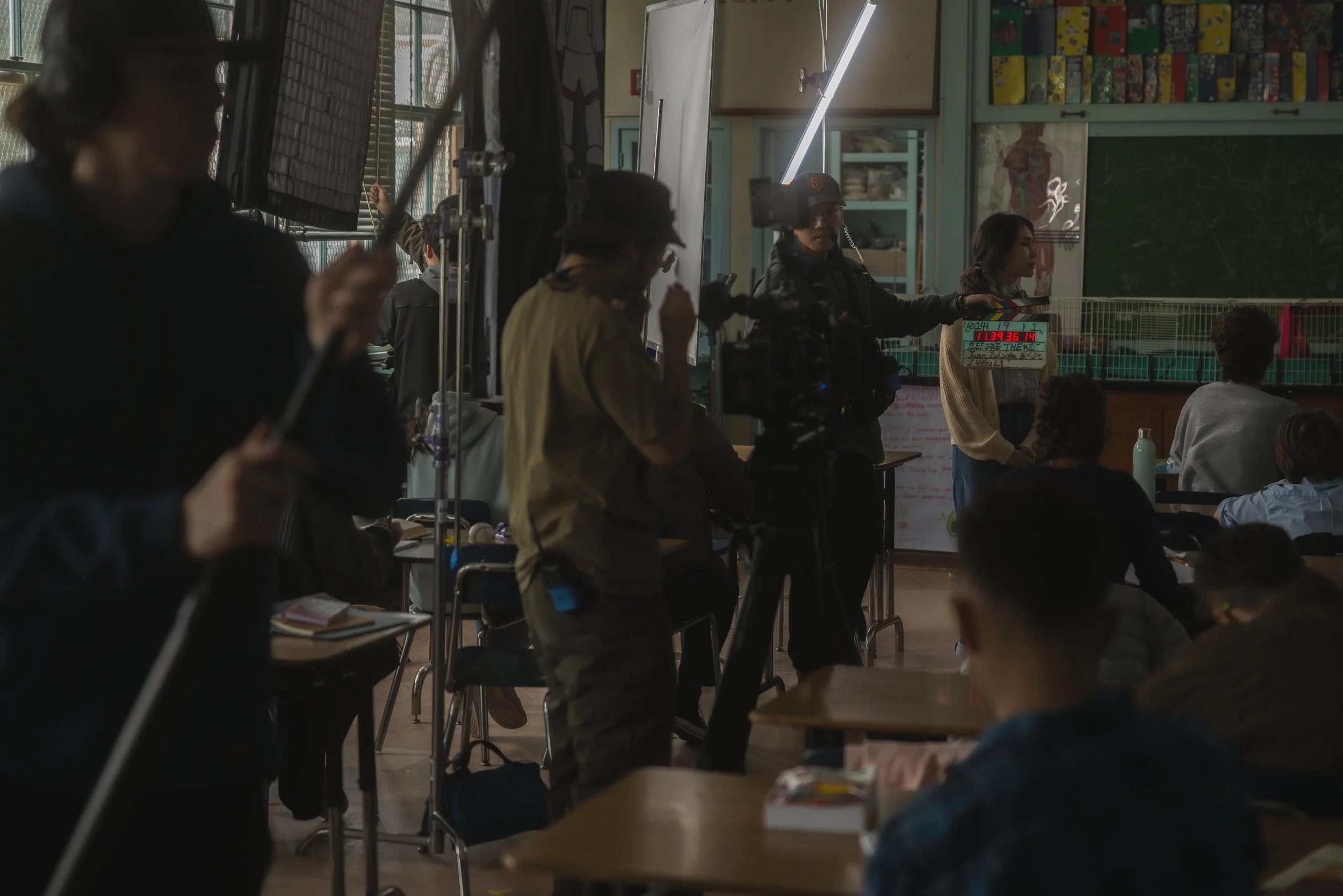 Film crew filming inside a classroom with students, equipment, and a teacher or presenter at the blackboard.