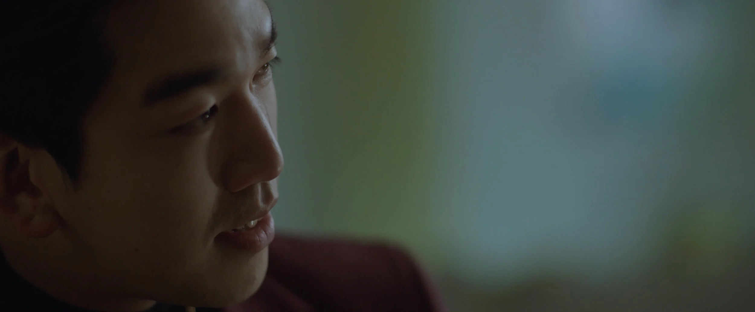 Close-up side profile of a young man with dark hair, looking contemplative, with a blurred gradient background.