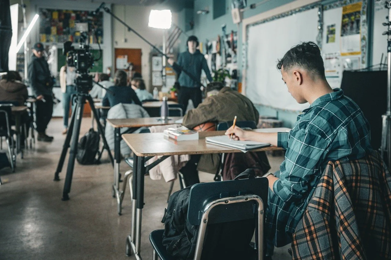 Students in a classroom filmmaking or media production setting, with a camera and crew filming a scene or conducting an interview.
