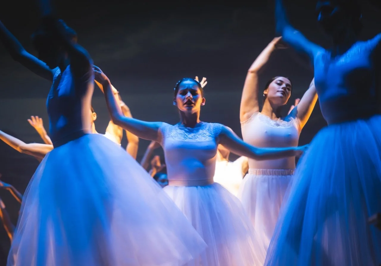 Ballet dancers in white tutus performing on stage under blue lighting.