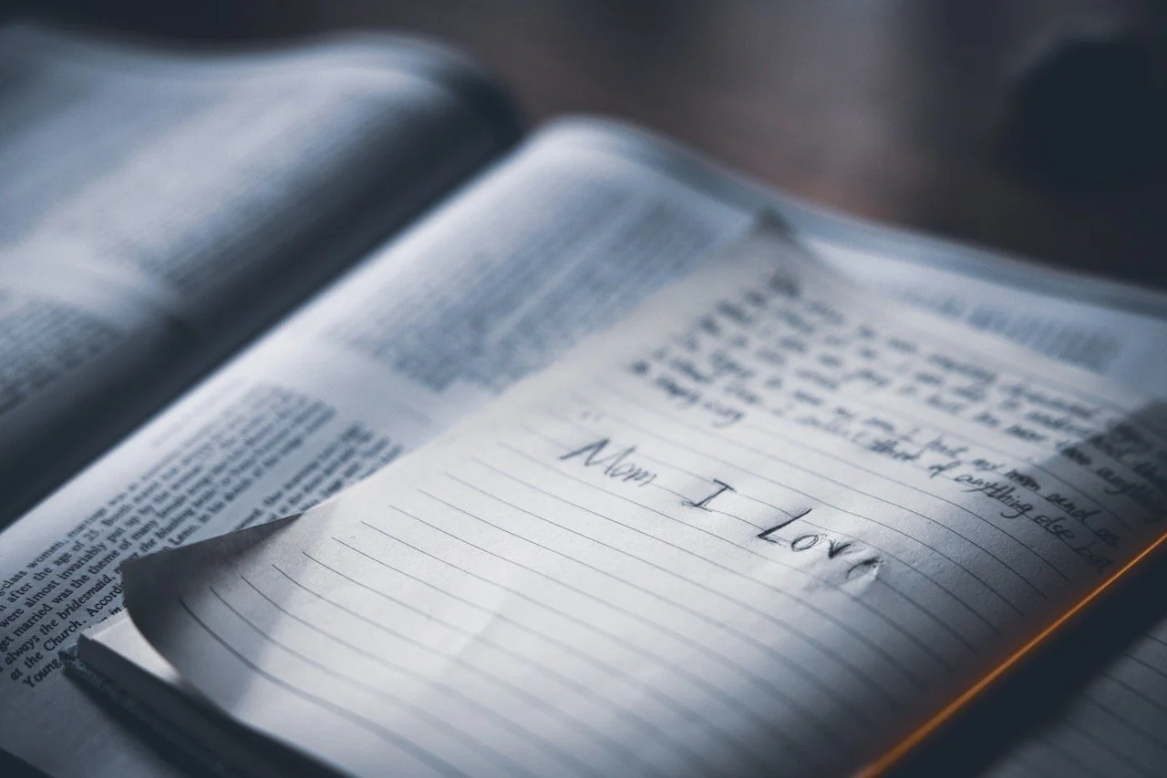 Open Bible with a handwritten note on lined paper that says, 'Mom I Love' inside the book.