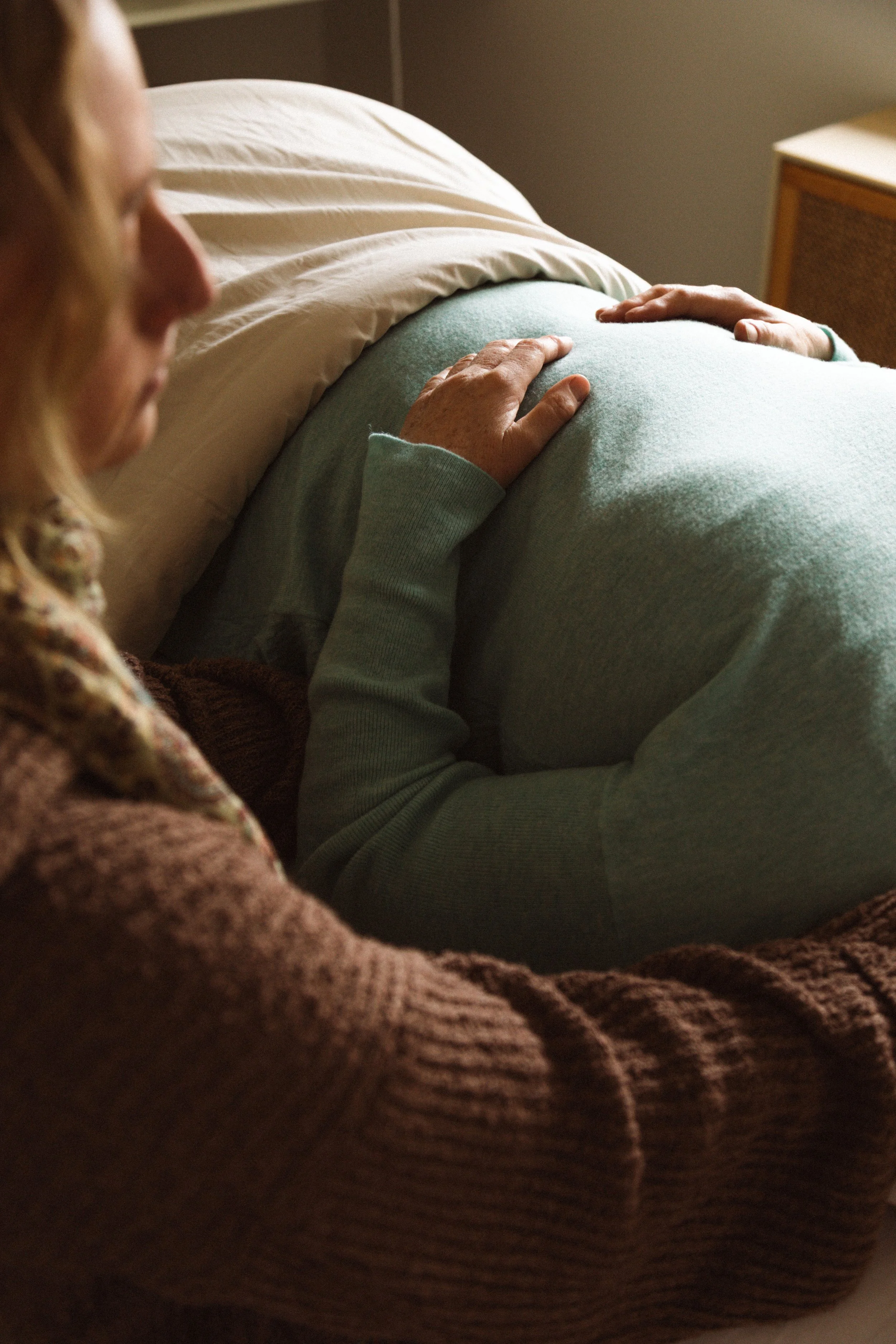 A person with long hair touching their pregnant belly.