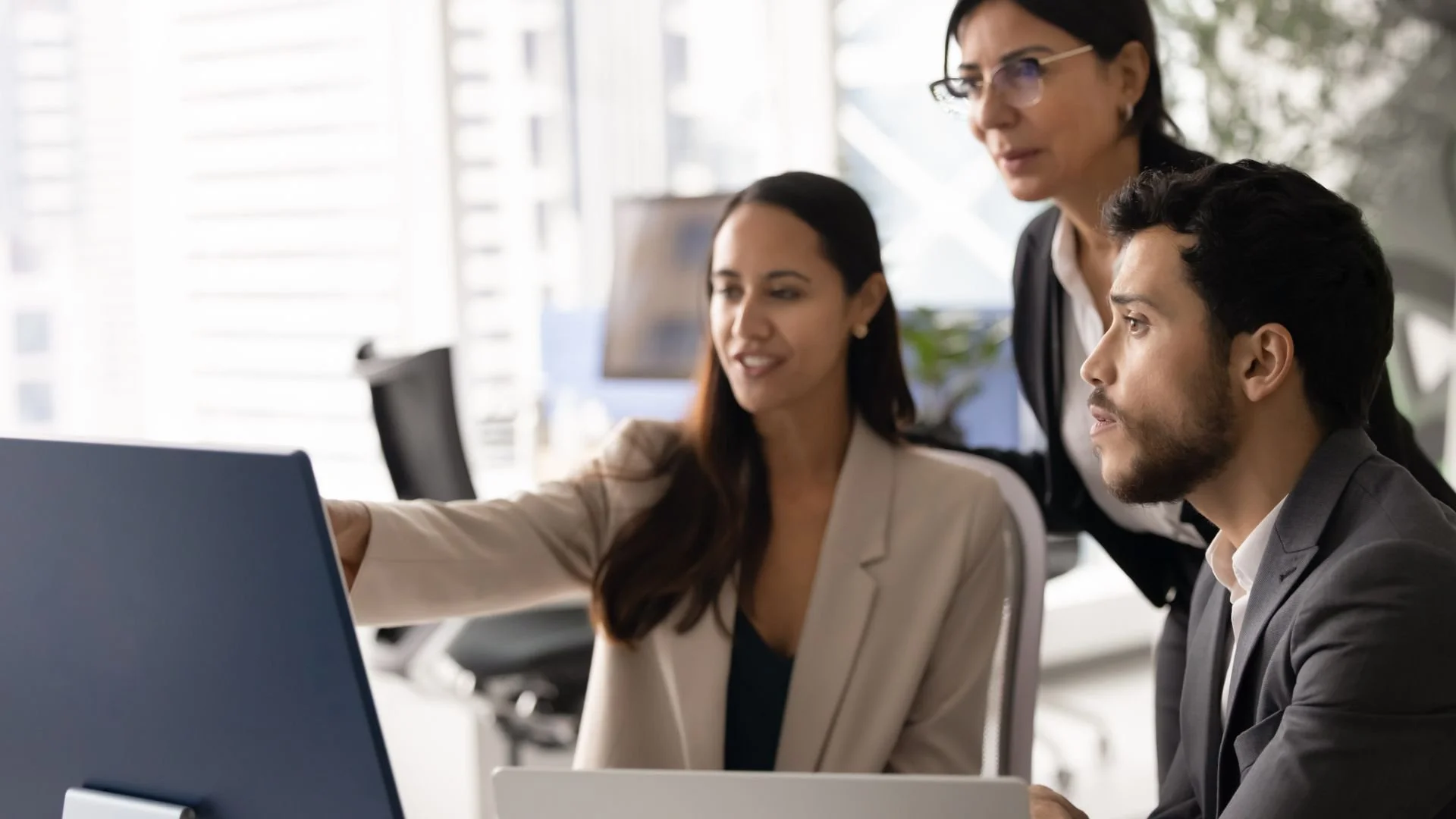 Three colleagues collaborate on a project in a modern office, with two women and one man focused on a laptop.