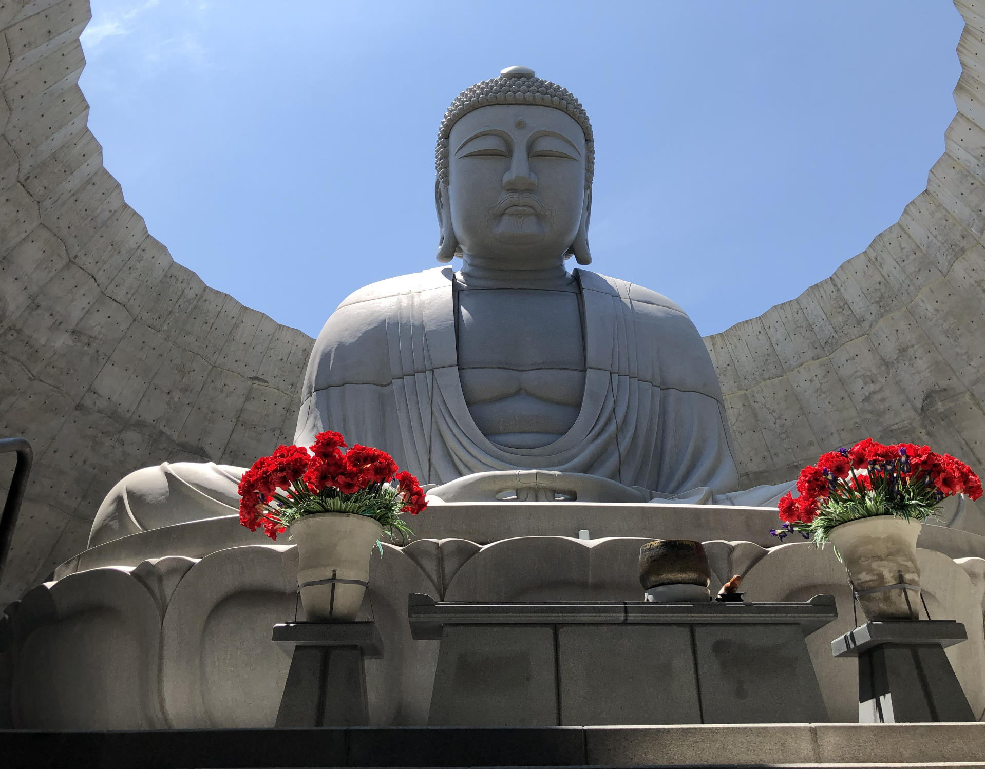 Hill of the Buddha, con flores rojas en macetas delante y un fondo de cielo azul.Hokkaido