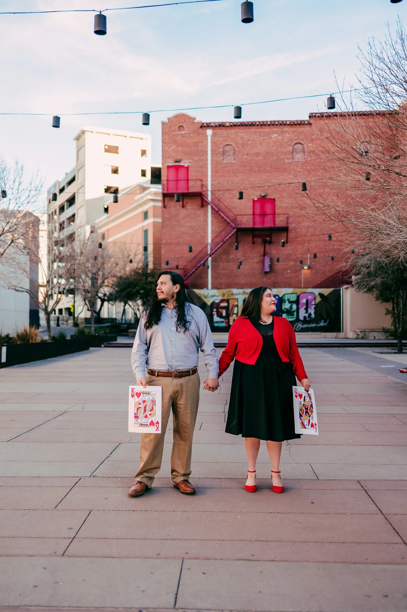 Couple smiling while holding oversized playing cards during a creative engagement session in downtown El Paso, Texas.